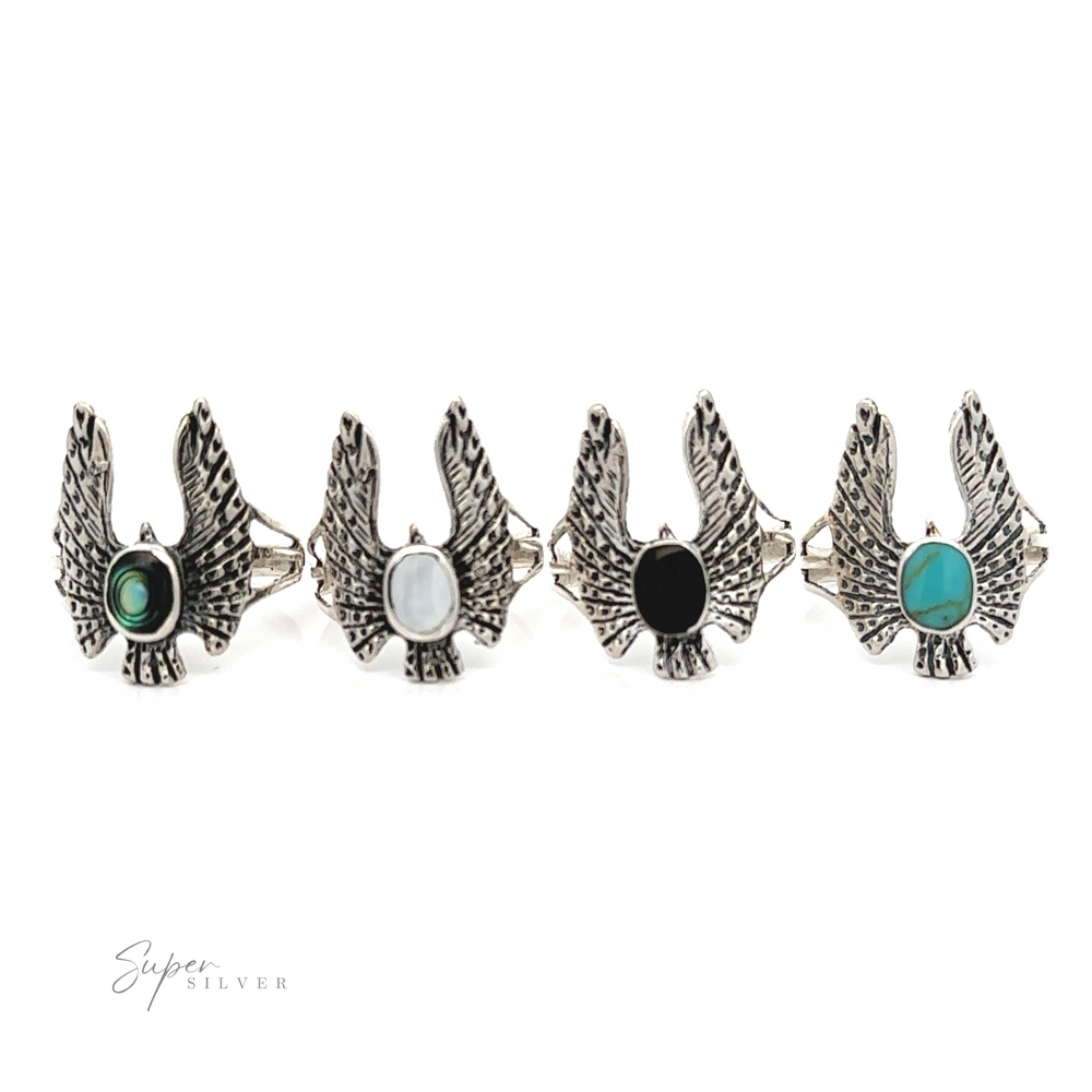 
                  
                    Four silver Inlaid Stone Rings with Eagle Wings, each with a different colored gemstone, displayed in a line against a white background.
                  
                