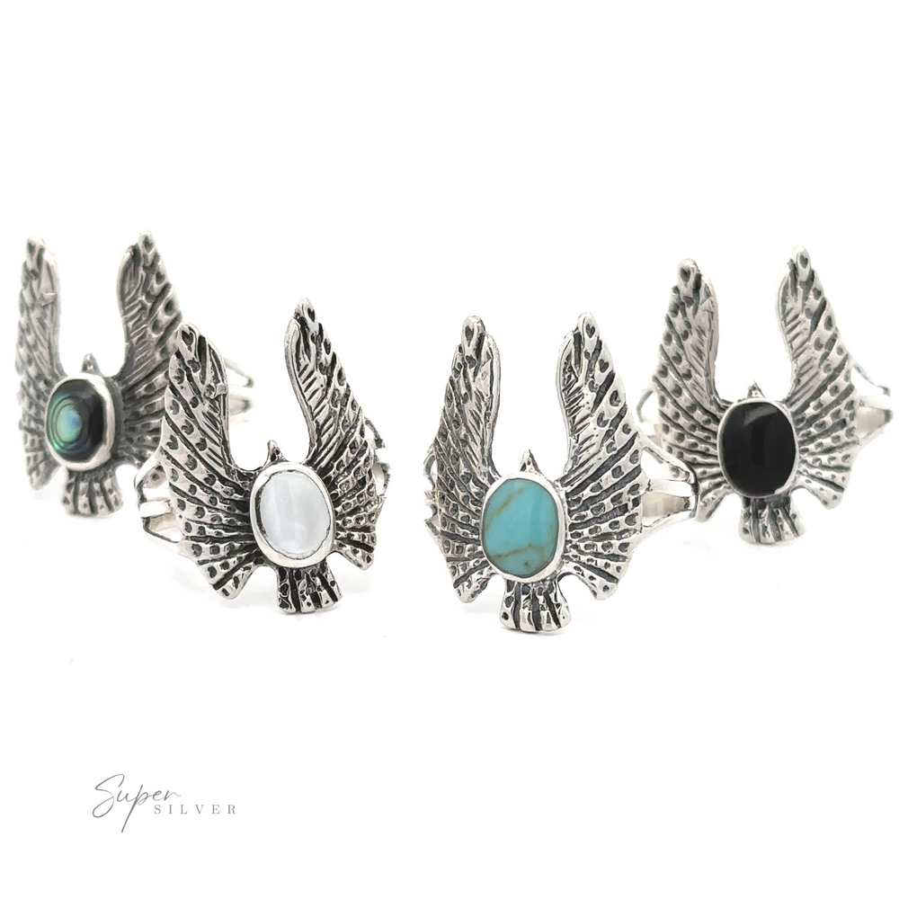 Four silver Inlaid Stone Rings with Eagle Wings displayed in a row, each with a different colored stone (green, white, turquoise, black) in the center.