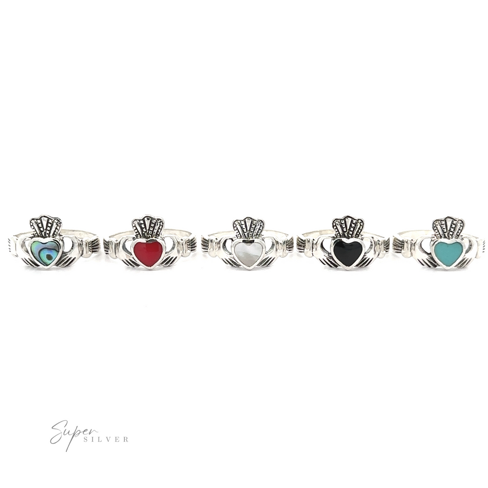 A series of five silver Claddagh Inlaid Stone Rings, representing Irish heritage, with varying heart colors including blue, red, white, black, and light blue, displayed against a white background.