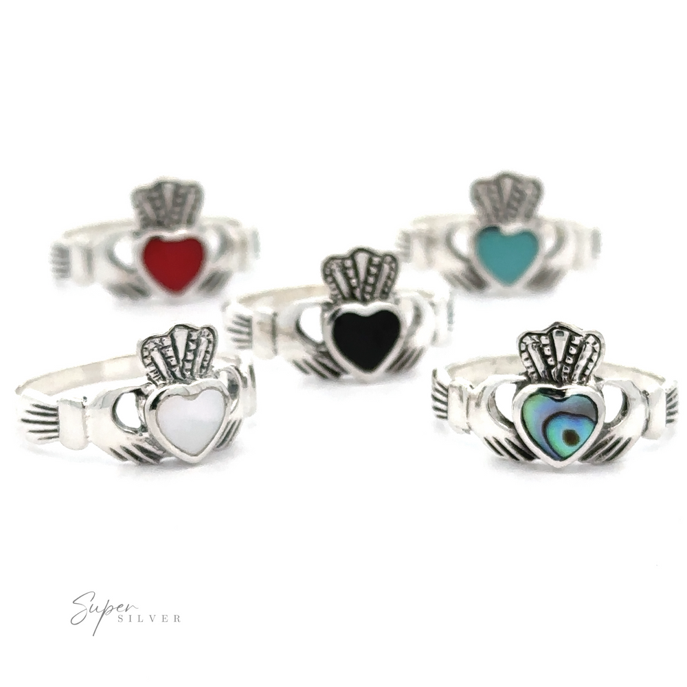 Five Claddagh Inlaid Stone Rings, representing Irish heritage, with varying heart colors (red, teal, black, white, and iridescent) displayed against a white background.
