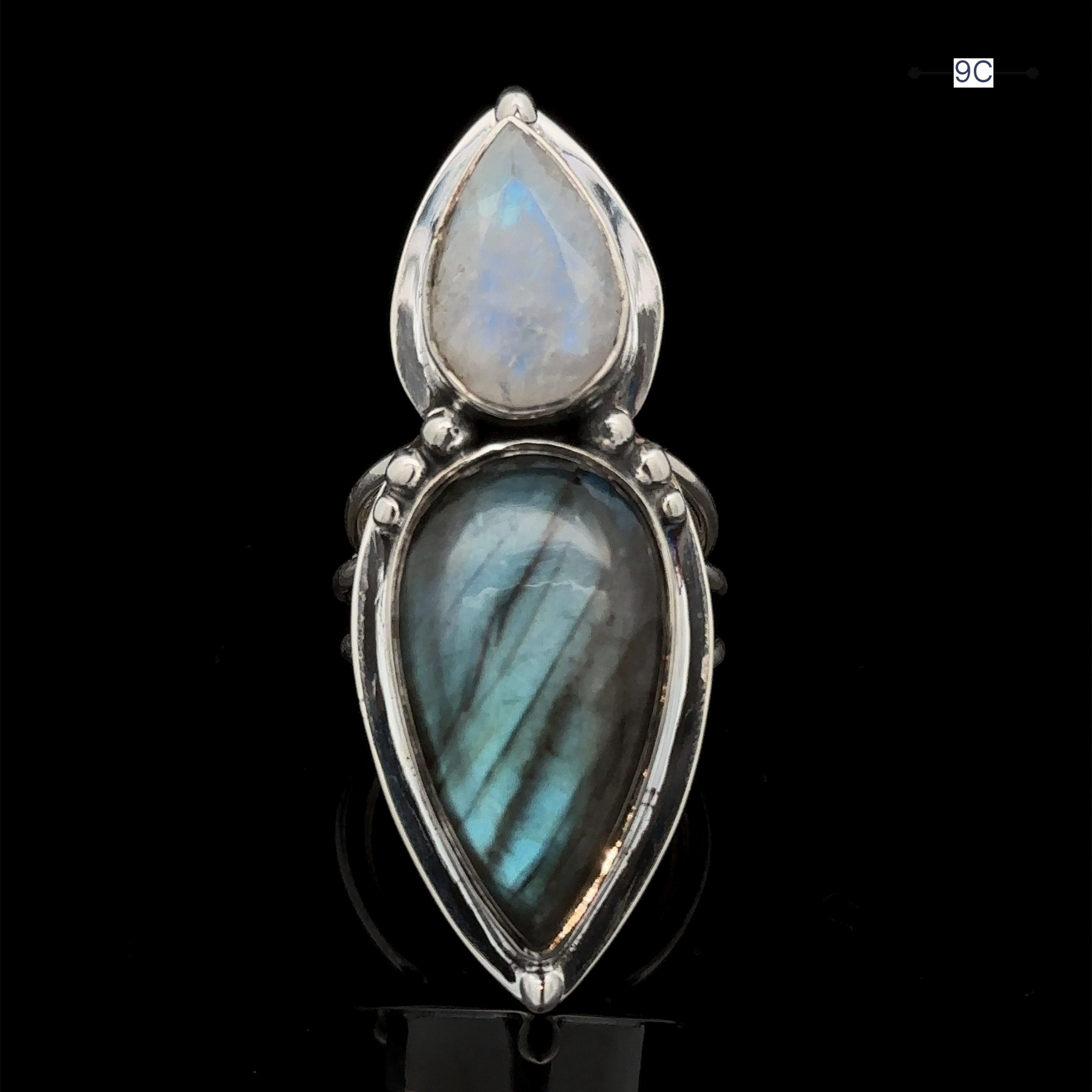 Introducing the Heavy Labradorite And Moonstone Ring, a captivating silver statement piece featuring two teardrop-shaped stones—a mesmerizing moonstone and a radiant labradorite—set against a dark background.