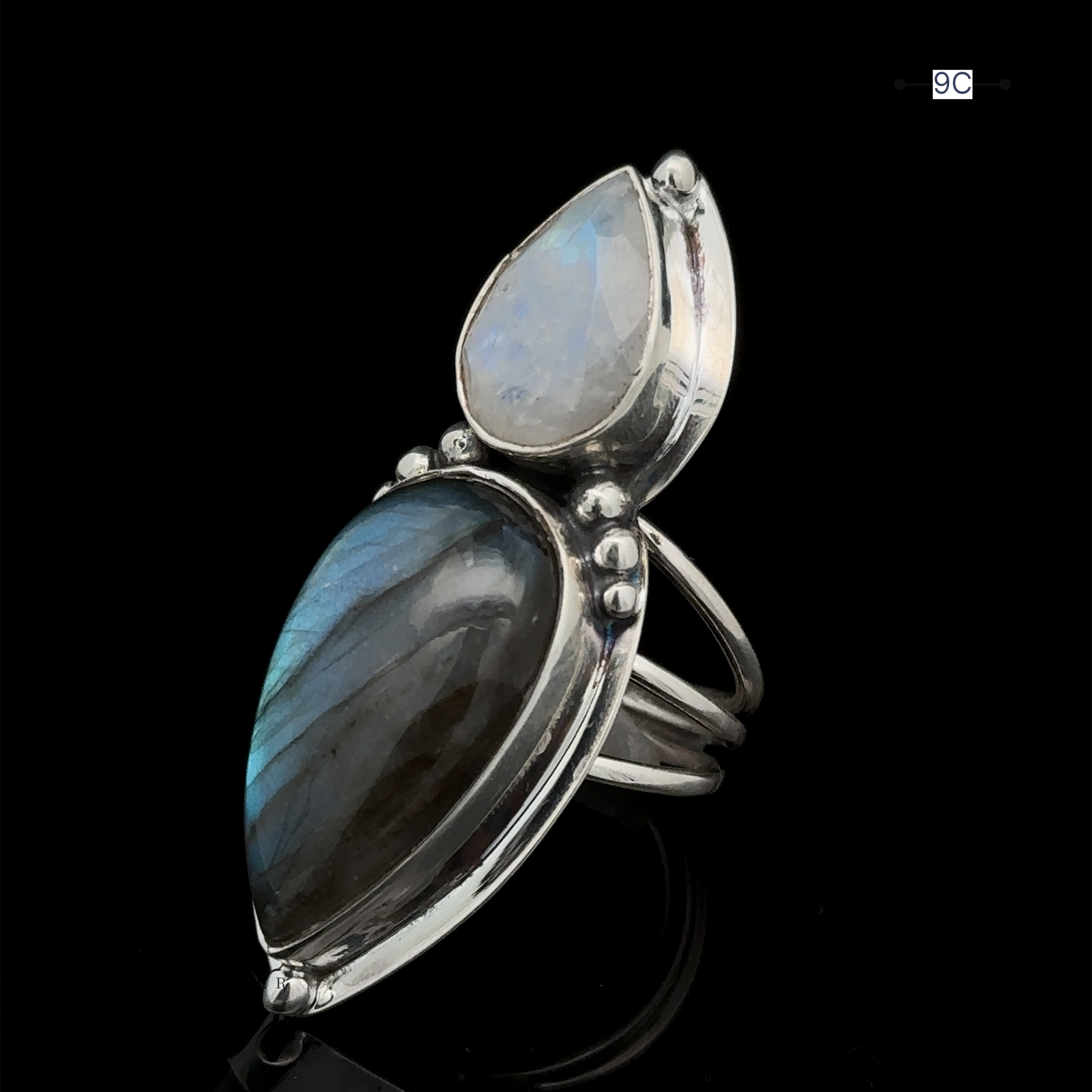 The Heavy Labradorite And Moonstone Ring, crafted from sterling silver, features a striking double stone setting with a large tear-shaped labradorite and a smaller teardrop-shaped moonstone, all showcased against a black background.