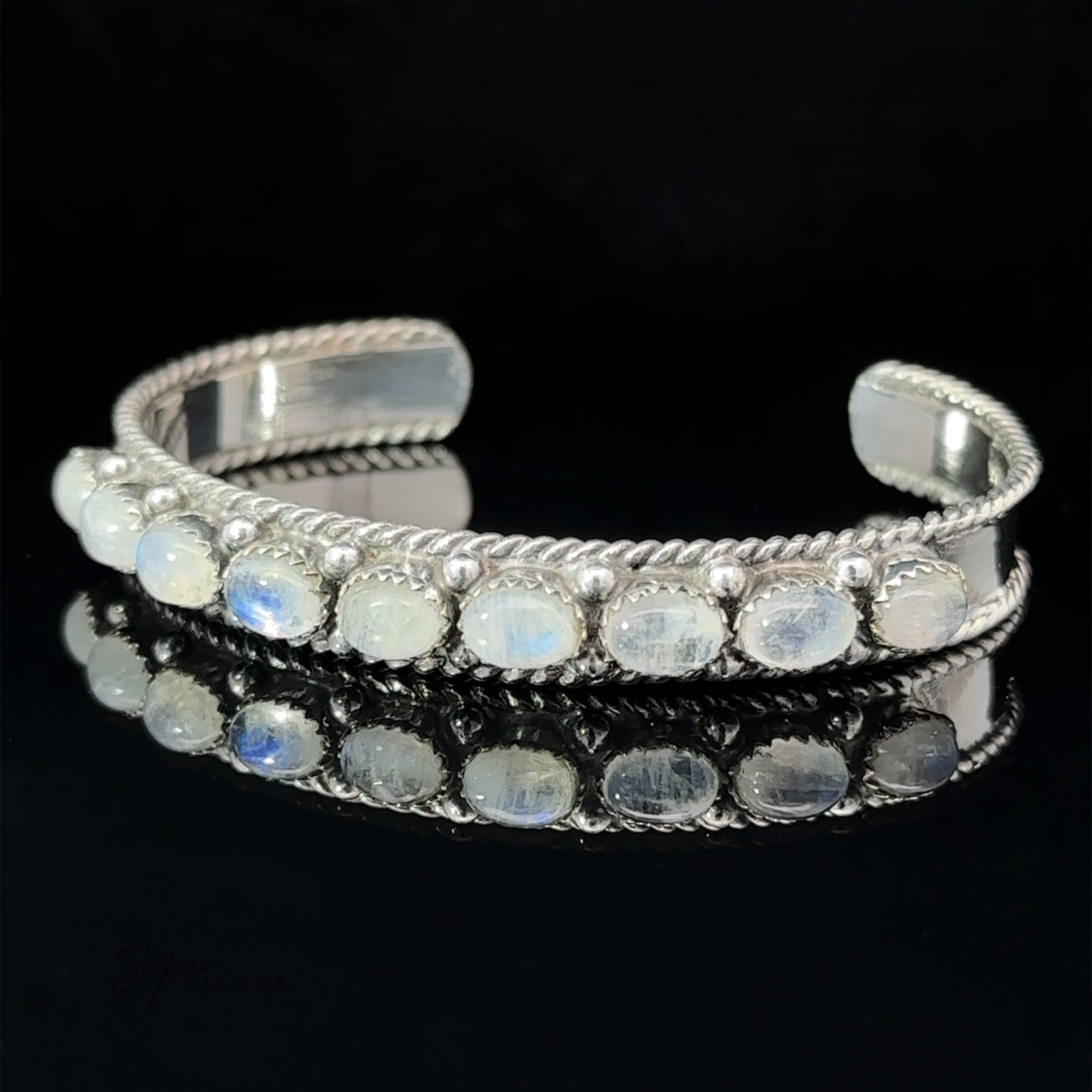 An Oval Moonstone Cuff Bracelet with a row of opalescent stones set along the top, displayed against a black background.