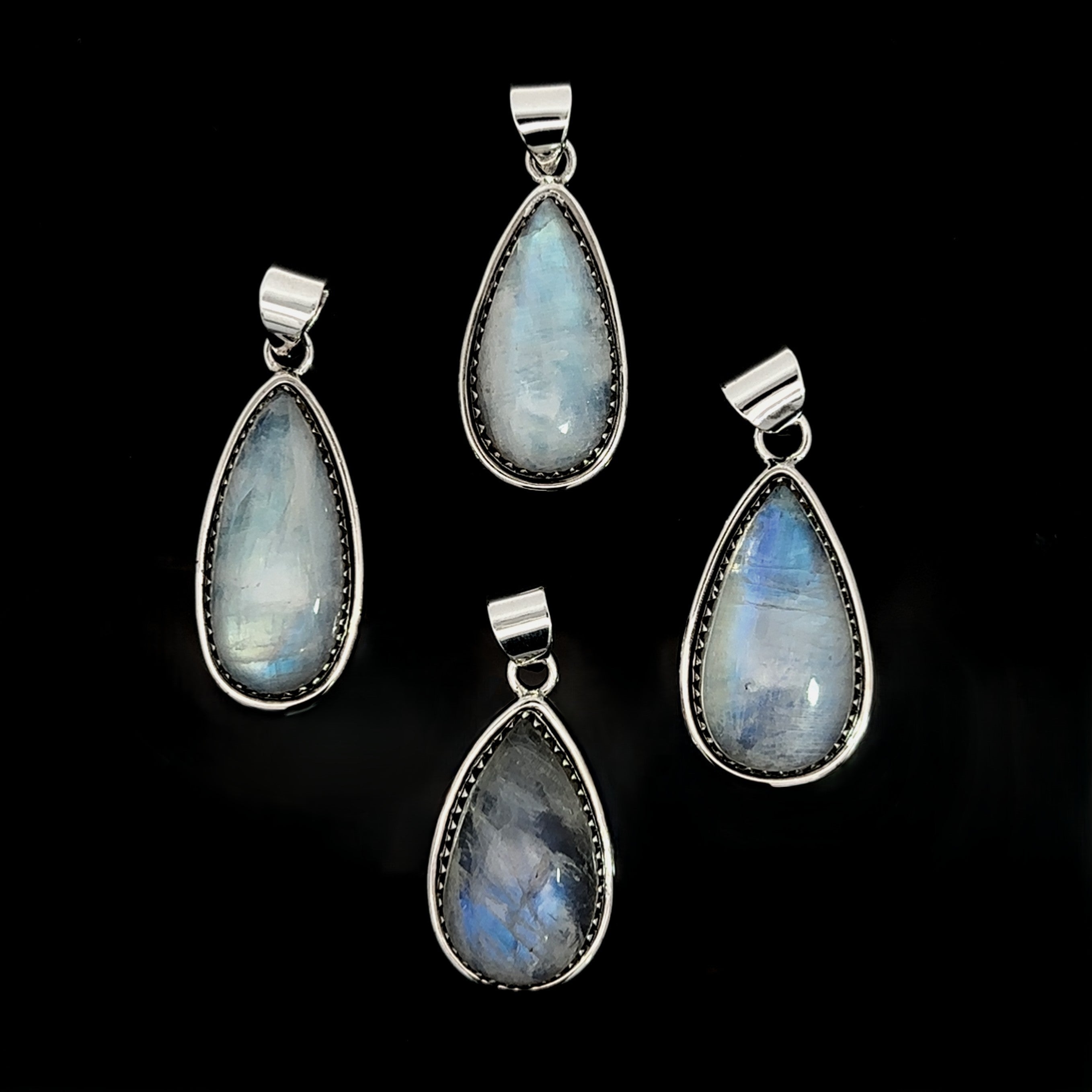 Four Teardrop Moonstone Pendants with sterling silver settings and boho detailing are displayed on a black background.