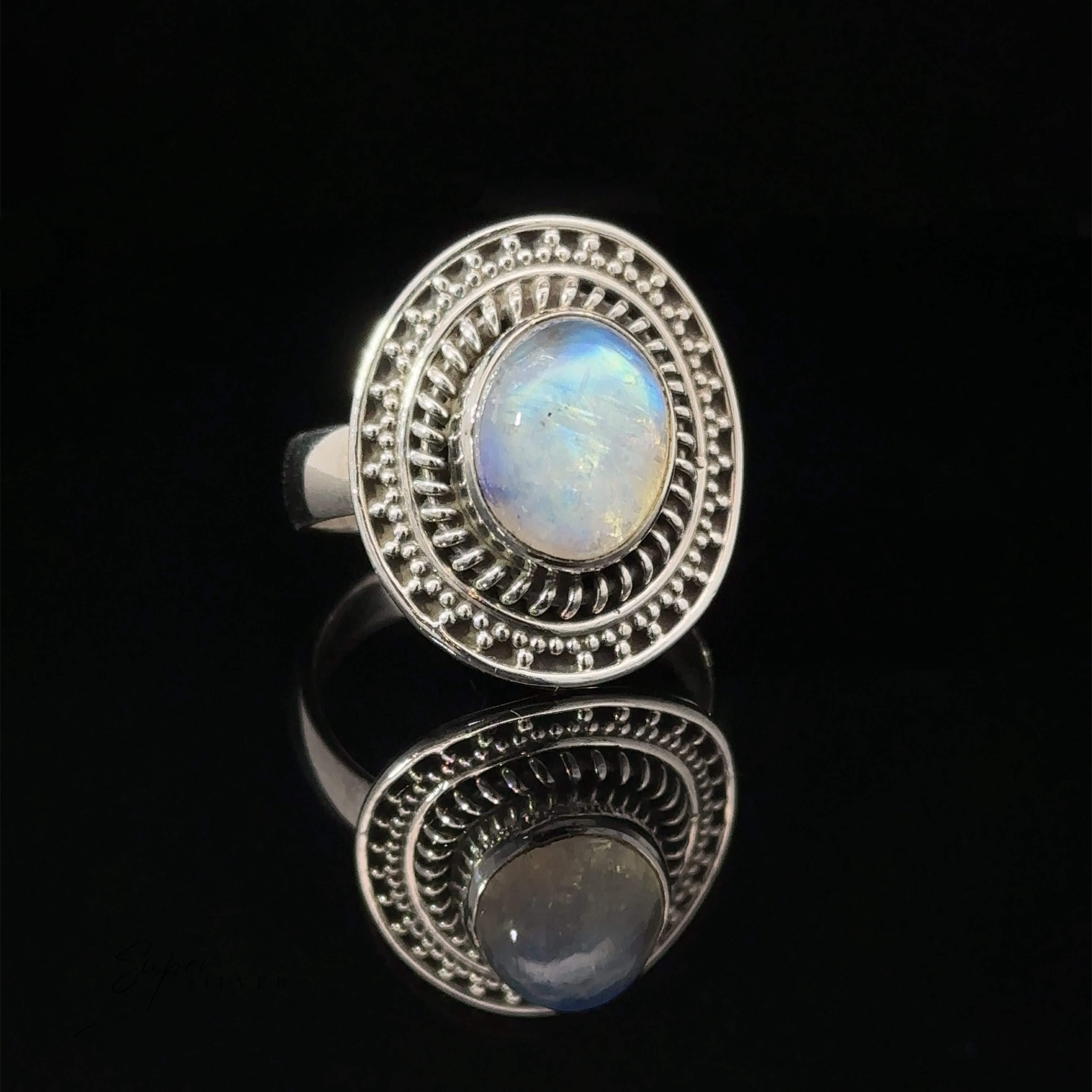 A moonstone ring with a braided disc design, displayed on a reflective black surface.