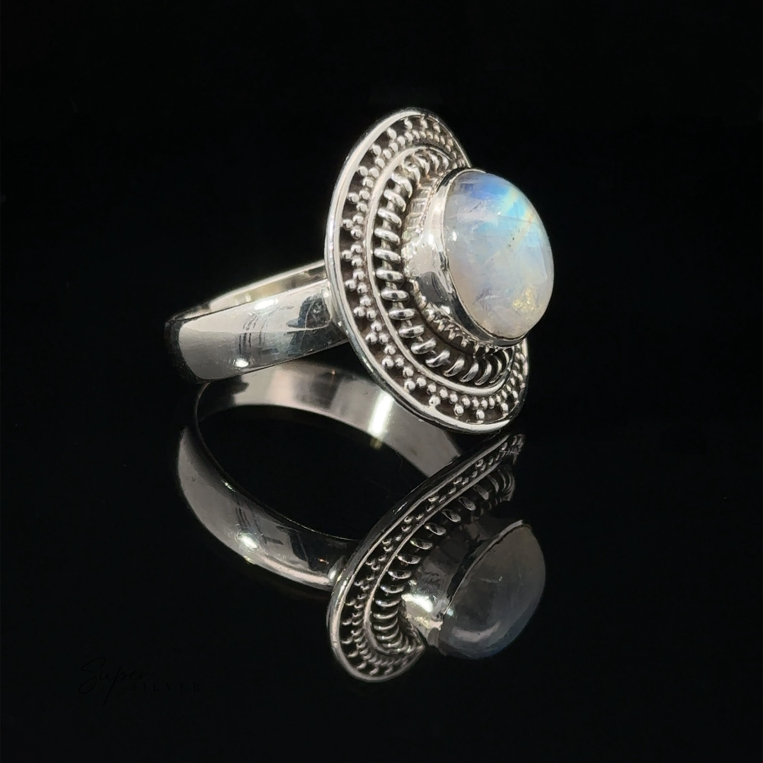 Moonstone Ring With Braided Disc Design, featuring a decorative border and set on a reflective surface.