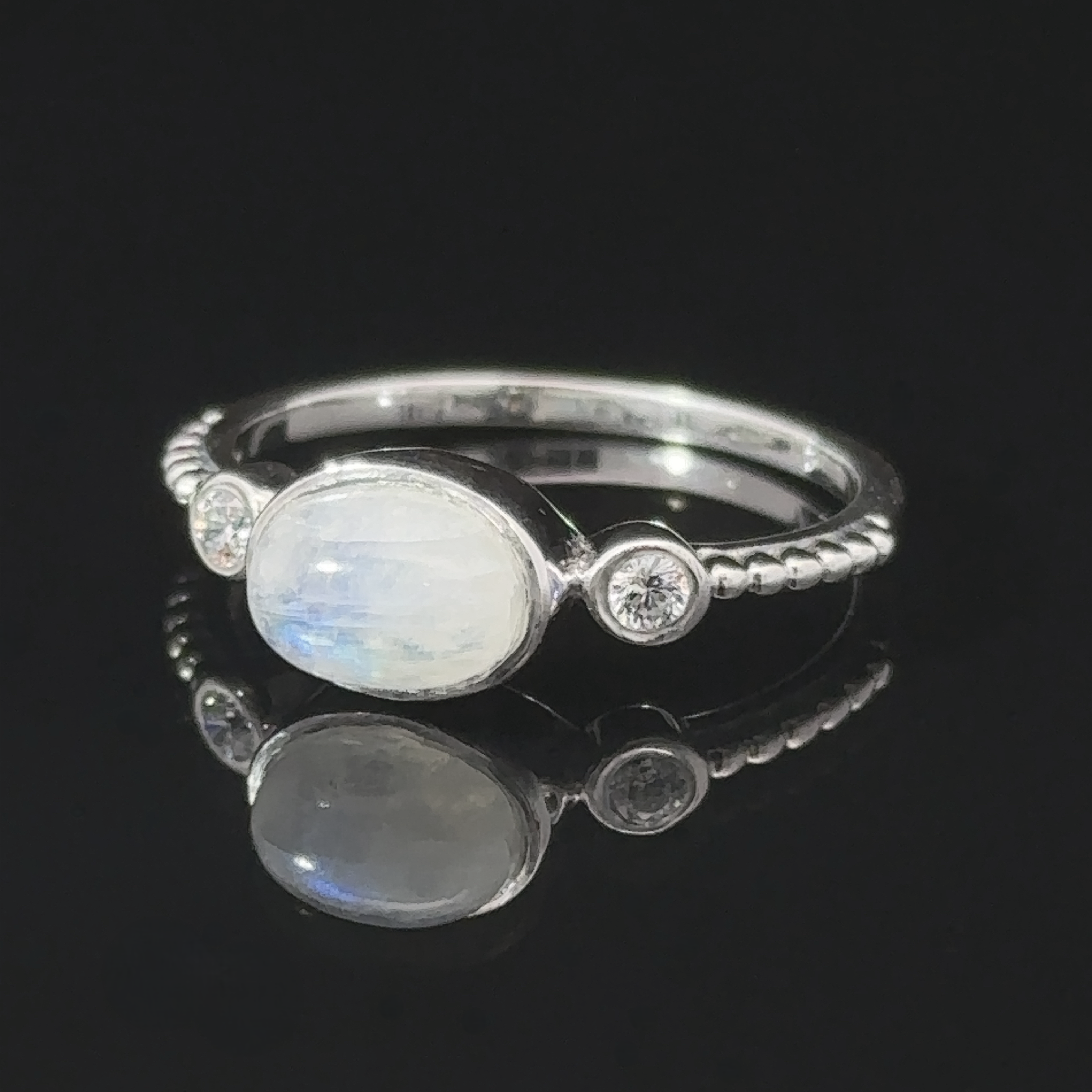 Handcrafted silver Horizontal Oval Gemstone Ring with Beaded Band and small diamonds, displayed on a reflective black surface.