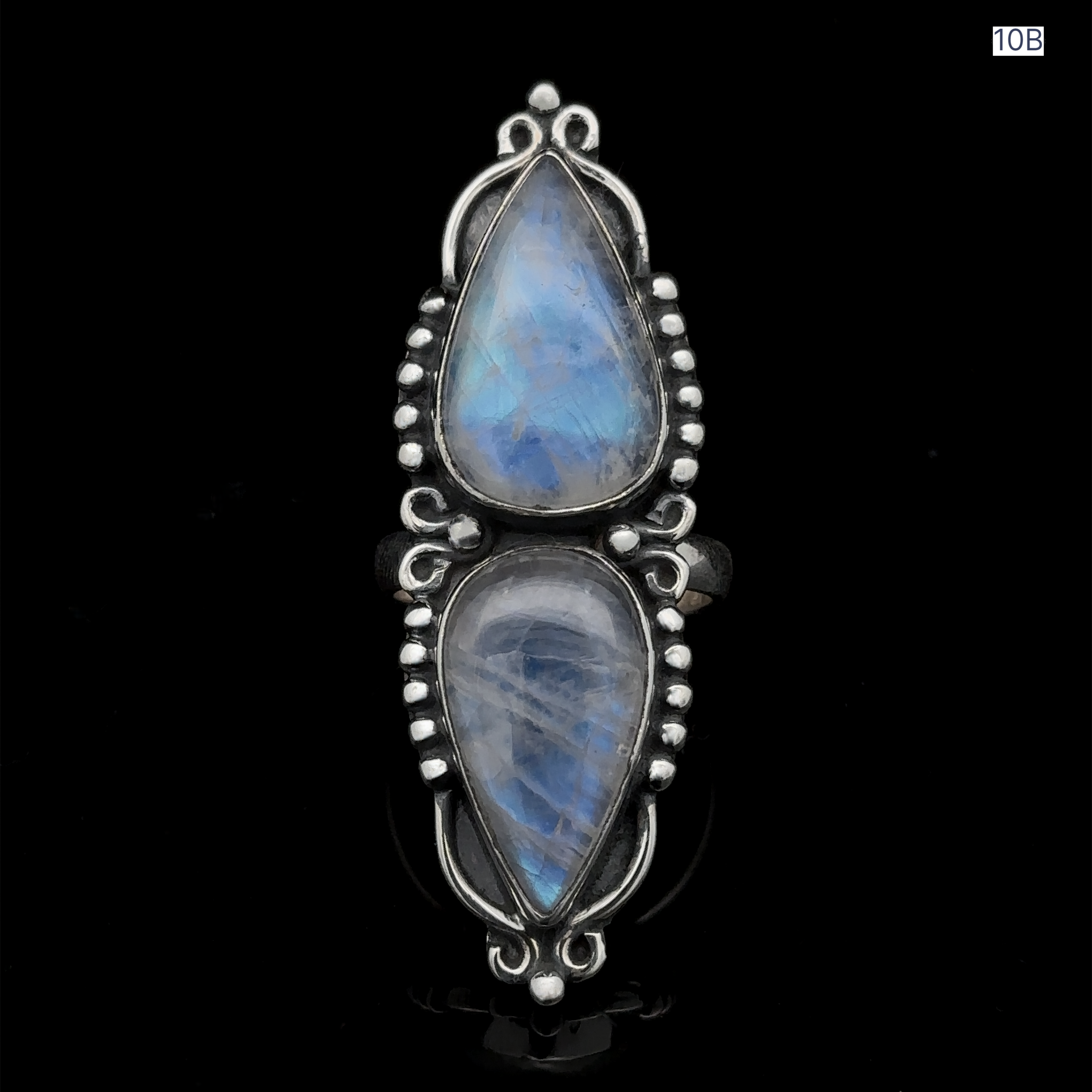 The Long Double Teardrop Moonstone Ring, crafted from sterling silver, features two vertically set pear-shaped moonstone gemstones and showcases intricate bead and swirl designs. It is elegantly displayed against a black background.