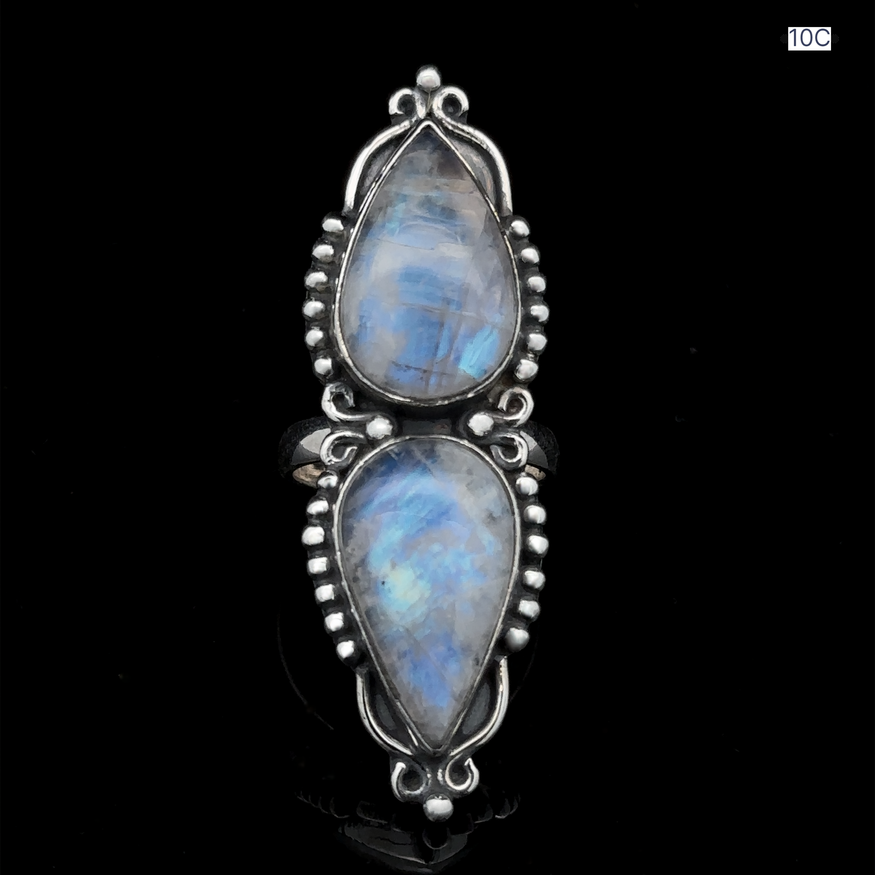 The Long Double Teardrop Moonstone Ring is a stunning statement piece, crafted from sterling silver and featuring two pear-shaped, blue-hued moonstones set vertically amidst intricate metalwork details, all against a black background.