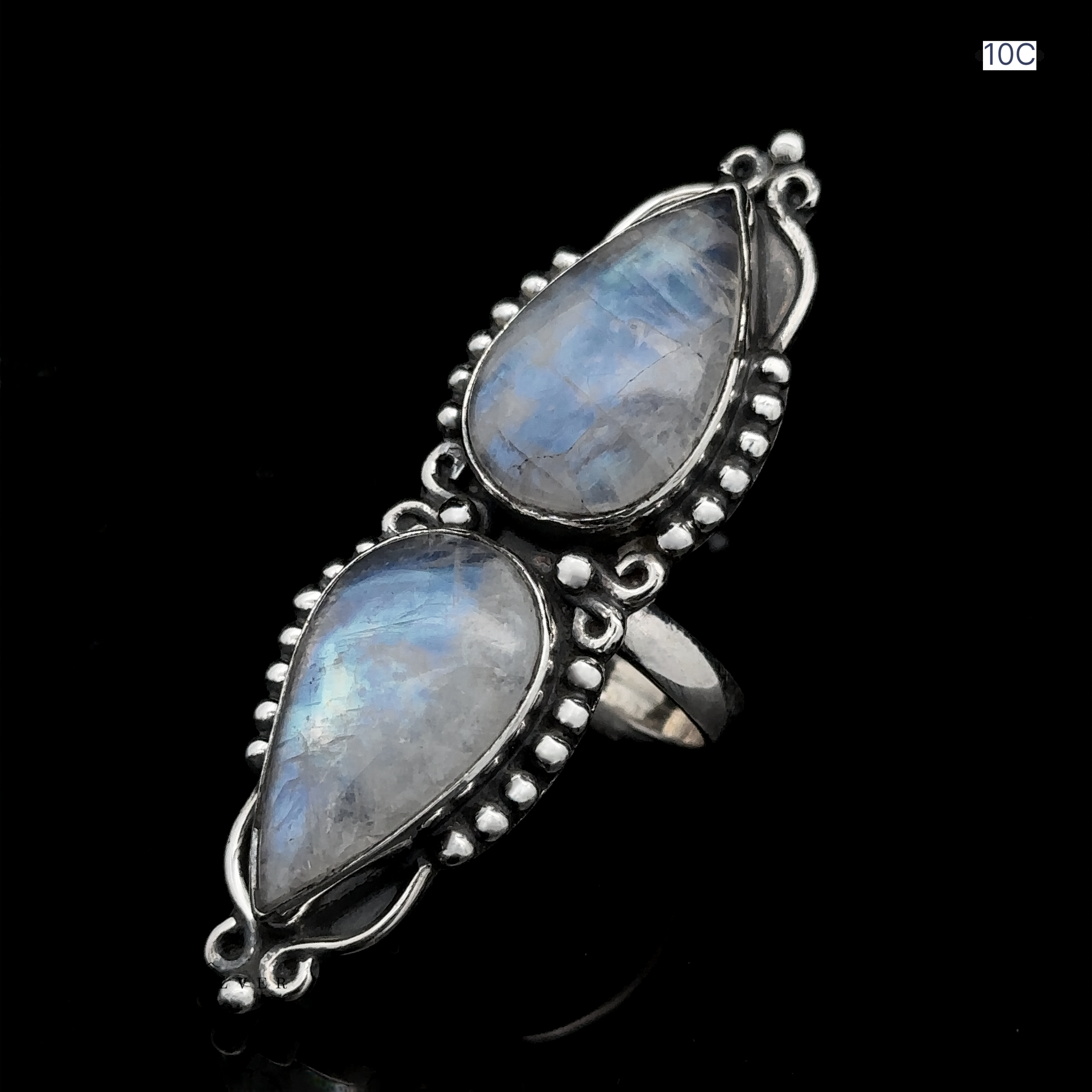 The Long Double Teardrop Moonstone Ring showcases two teardrop-shaped blue gemstones set in intricate decorative frames against a black background, making it a true statement piece.