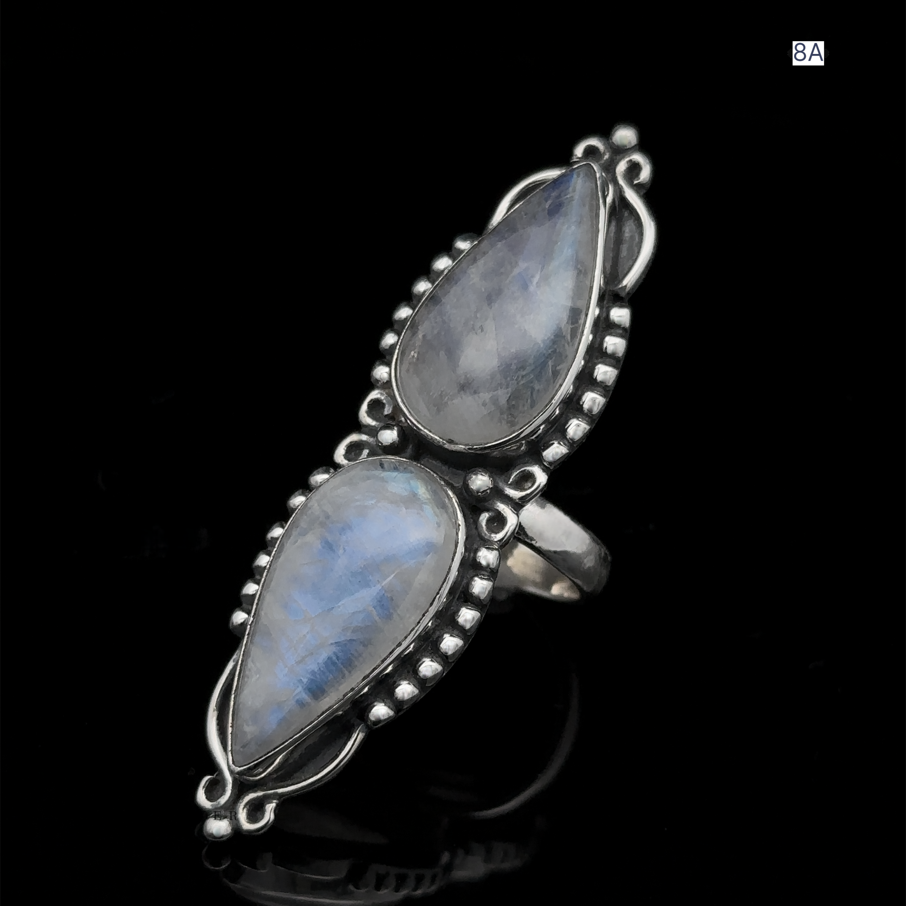 The Long Double Teardrop Moonstone Ring is a sterling silver statement piece, featuring two large teardrop-shaped moonstones, adorned with intricate silver beads and wire detailing, all set against a black background.