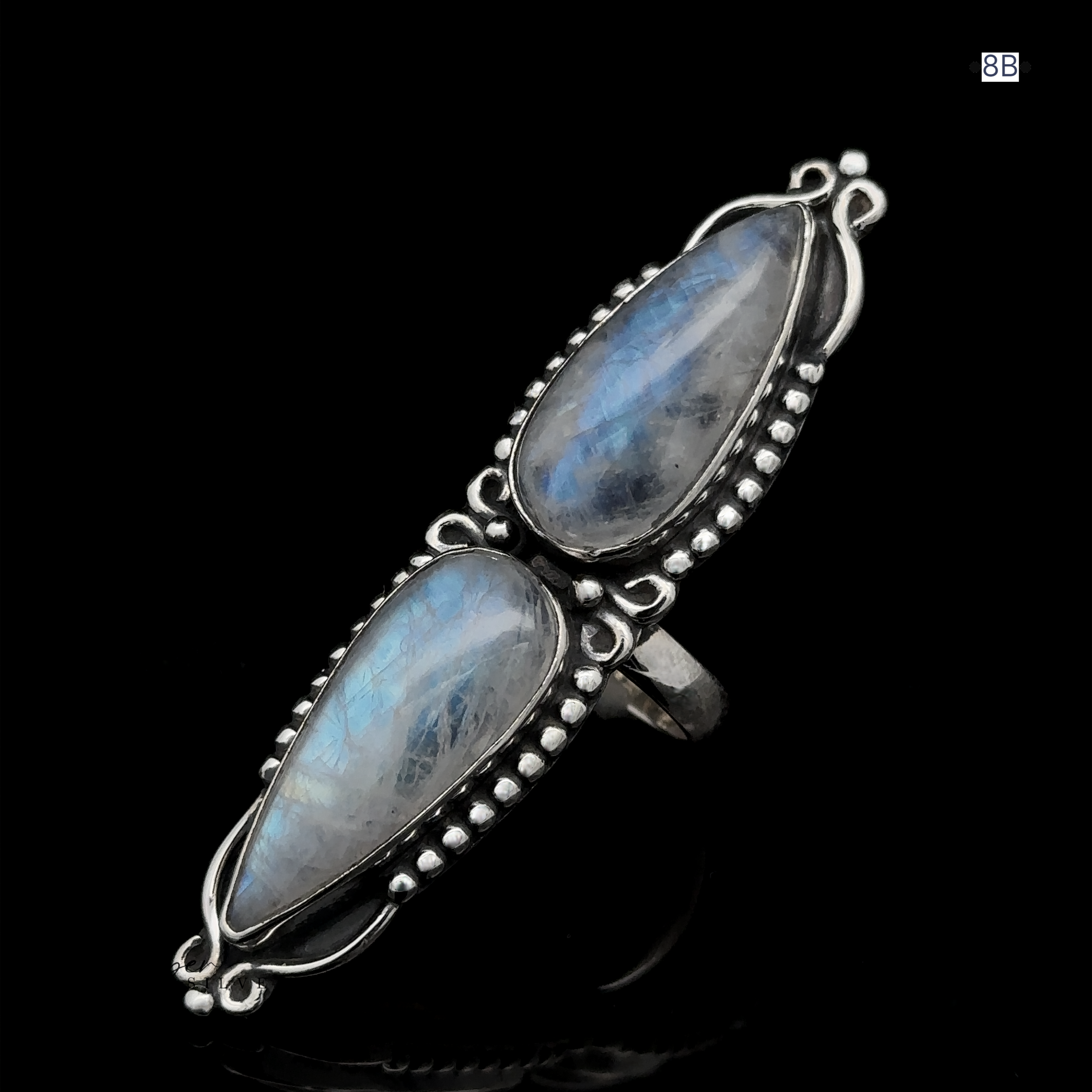 The Long Double Teardrop Moonstone Ring showcases two elongated oval moonstone gemstones set in sterling silver with decorative bead detailing against a black background. This statement ring encapsulates elegance and mystique in one stunning piece.