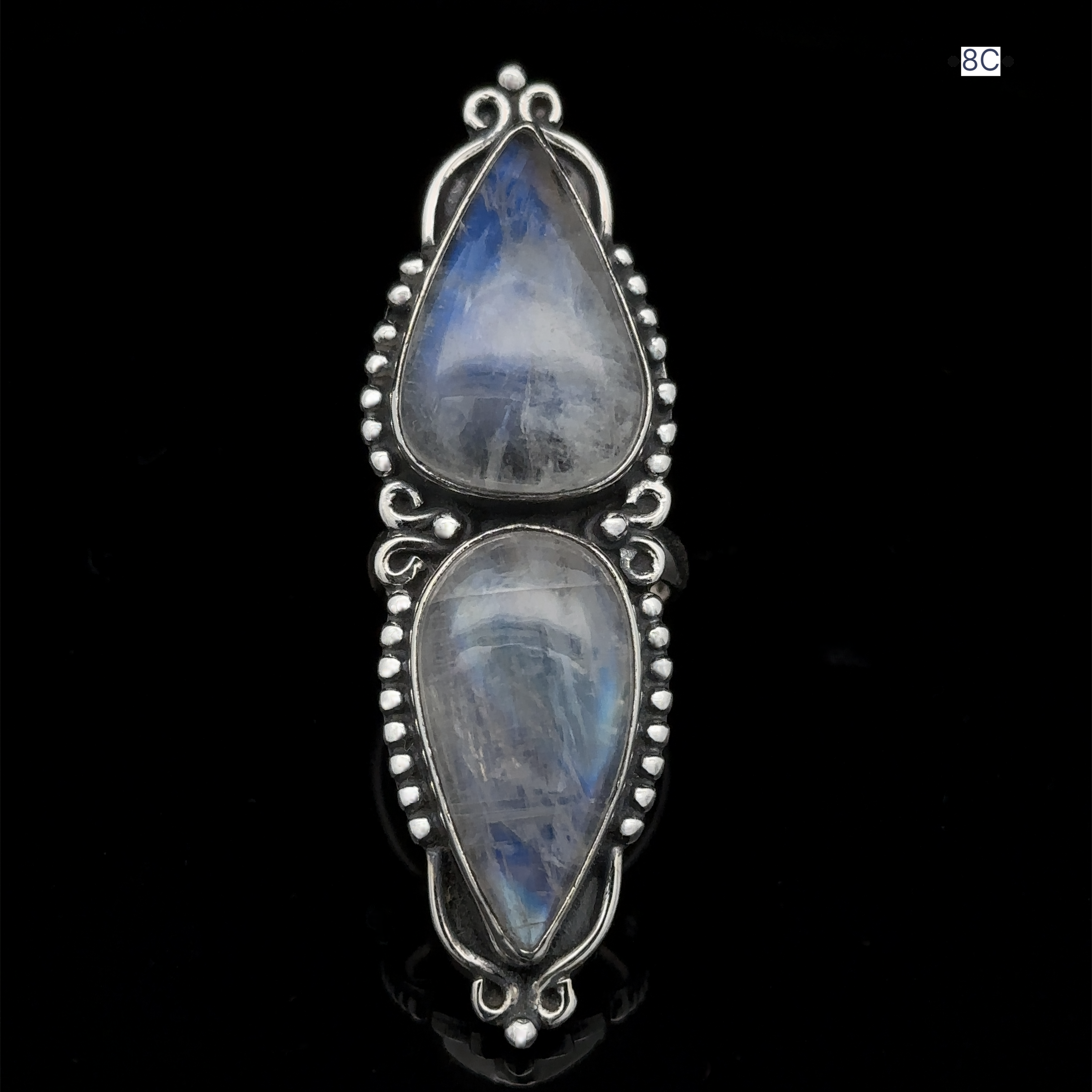 The Long Double Teardrop Moonstone Ring is crafted from sterling silver and features blue and white iridescent moonstones set in an ornate bezel on a black background.