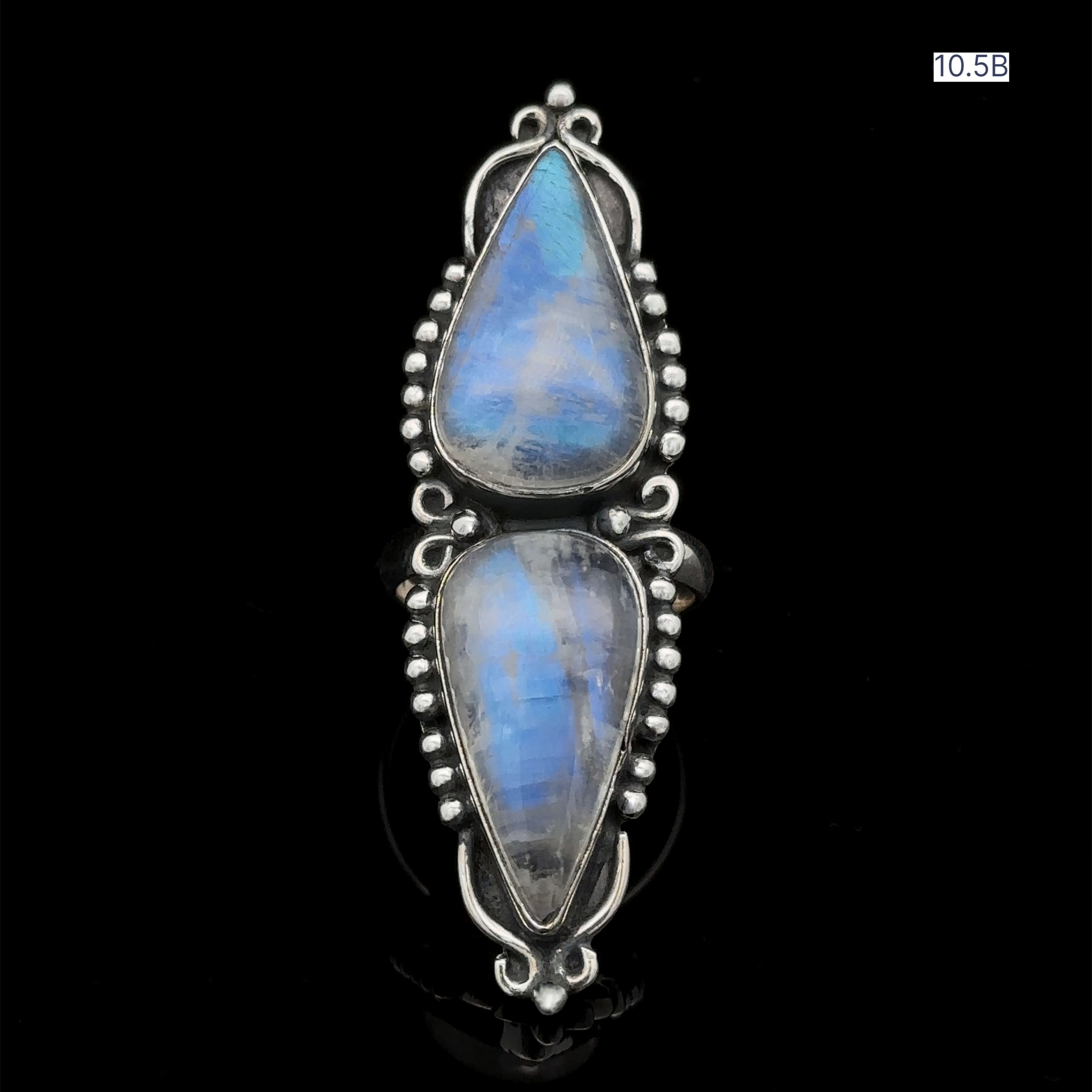 A statement ring called the Long Double Teardrop Moonstone Ring, featuring two vertically aligned, teardrop-shaped blue moonstones set in an intricate, decorative sterling silver setting against a black background.