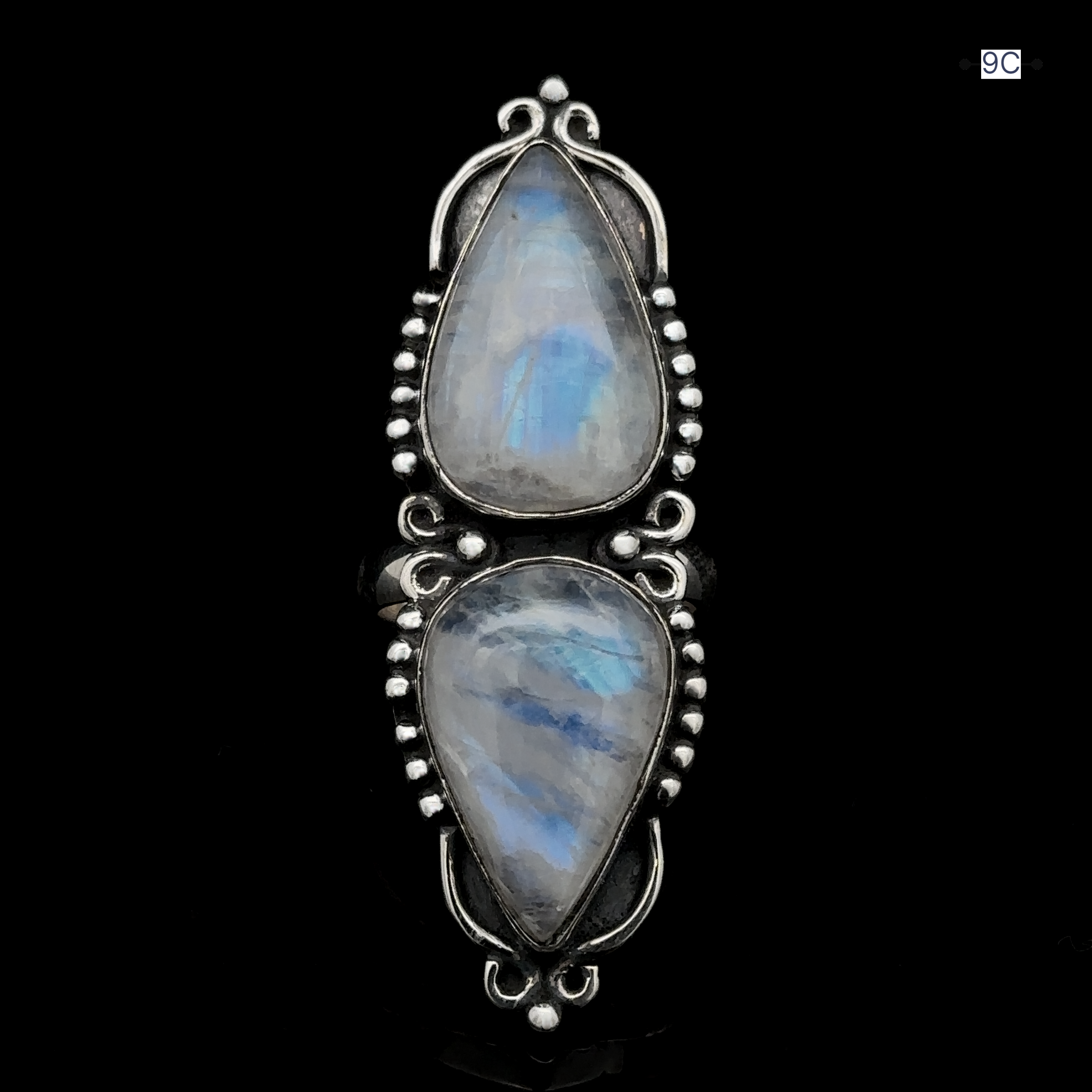 The Long Double Teardrop Moonstone Ring is an ornate sterling silver statement piece featuring two teardrop-shaped moonstone gems, adorned with intricate bead and filigree designs on a black background.