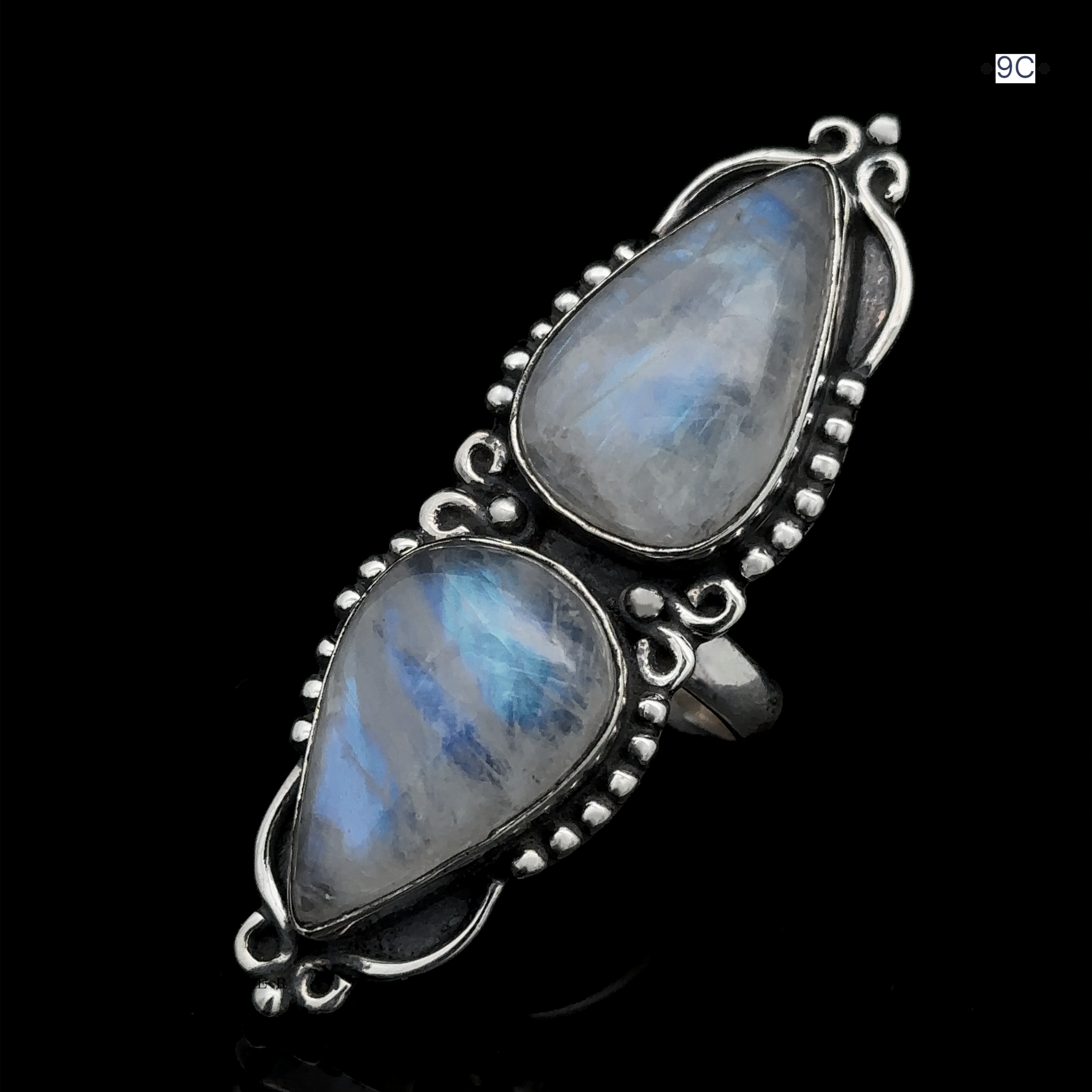 The Long Double Teardrop Moonstone Ring, crafted from sterling silver and adorned with intricate metalwork and small bead details, features two vertically placed teardrop-shaped moonstones, displayed beautifully against a black background.