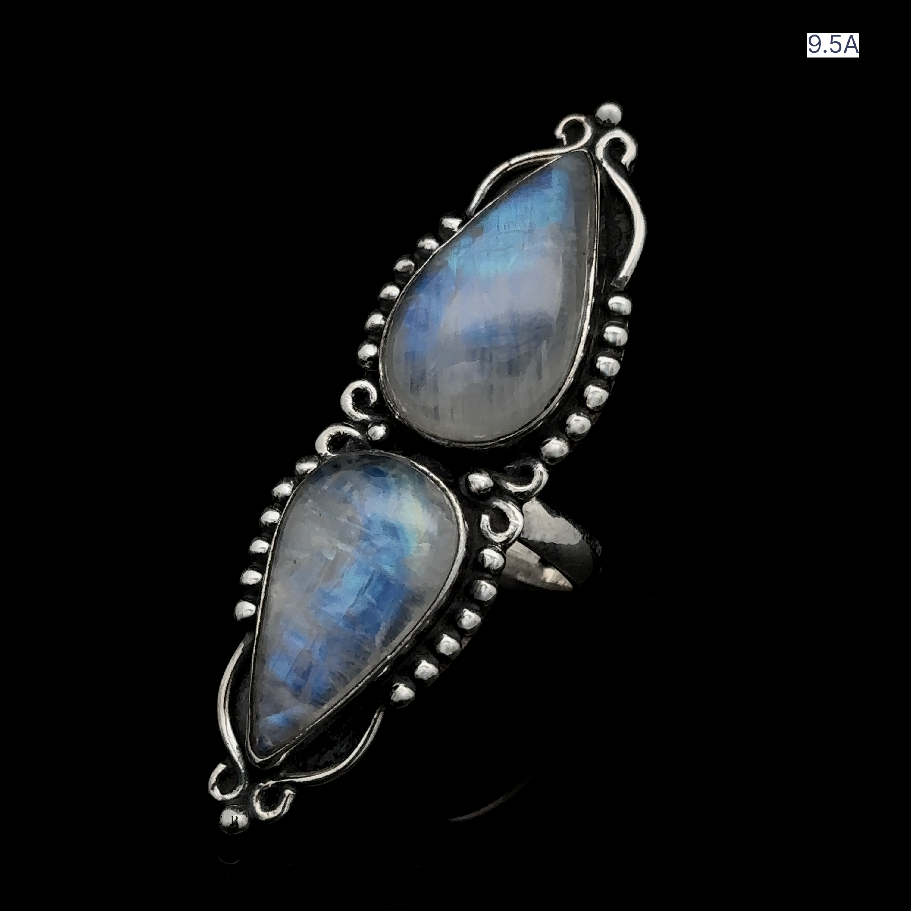 The Long Double Teardrop Moonstone Ring, a stunning sterling silver piece with two teardrop-shaped blue gemstones set vertically and adorned with bead-like details, is elegantly showcased on a black background. This statement ring exudes elegance and sophistication.