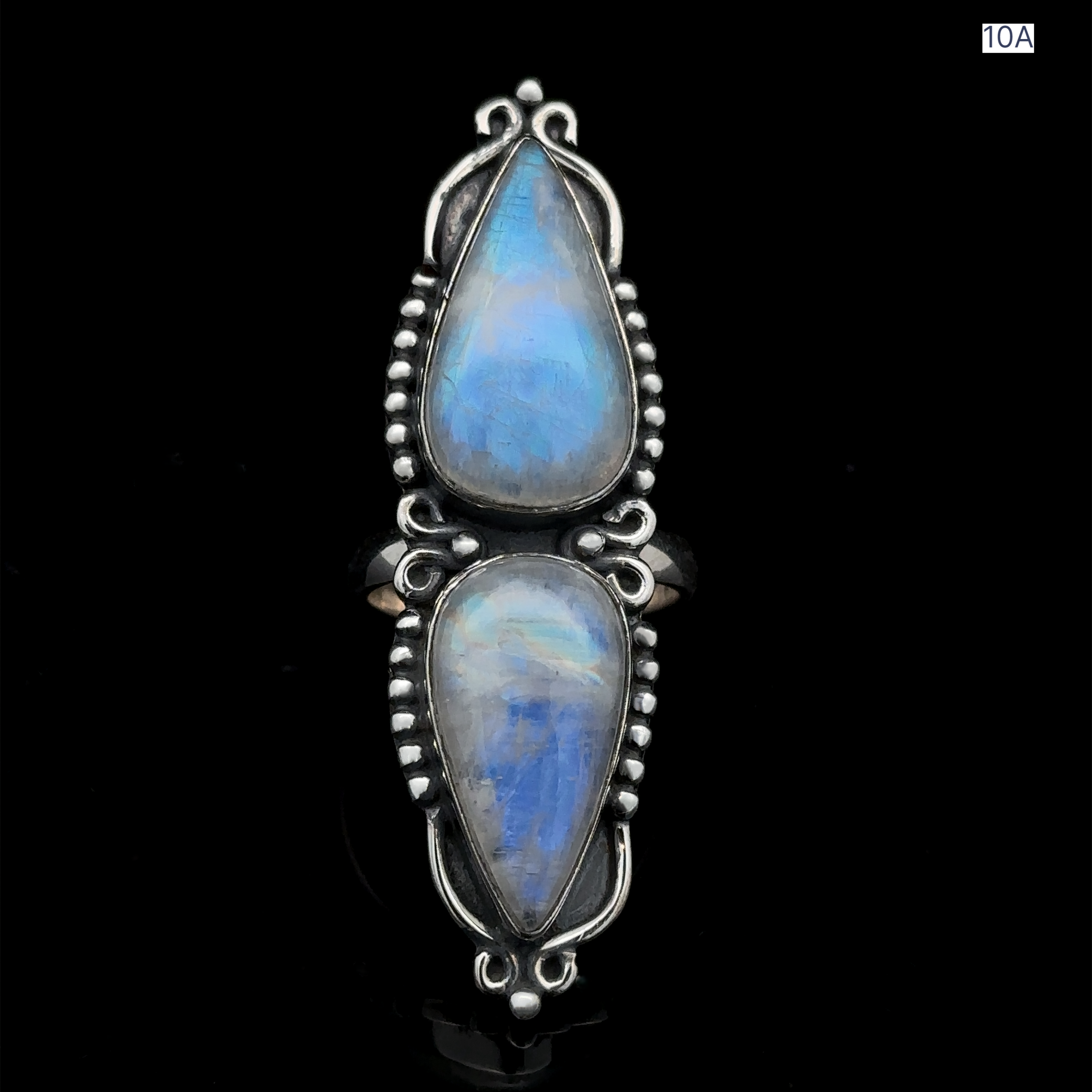 The Long Double Teardrop Moonstone Ring is a sterling silver statement piece showcasing two vertically-aligned, teardrop-shaped blue moonstones with intricate detailing, set against a plain black background.