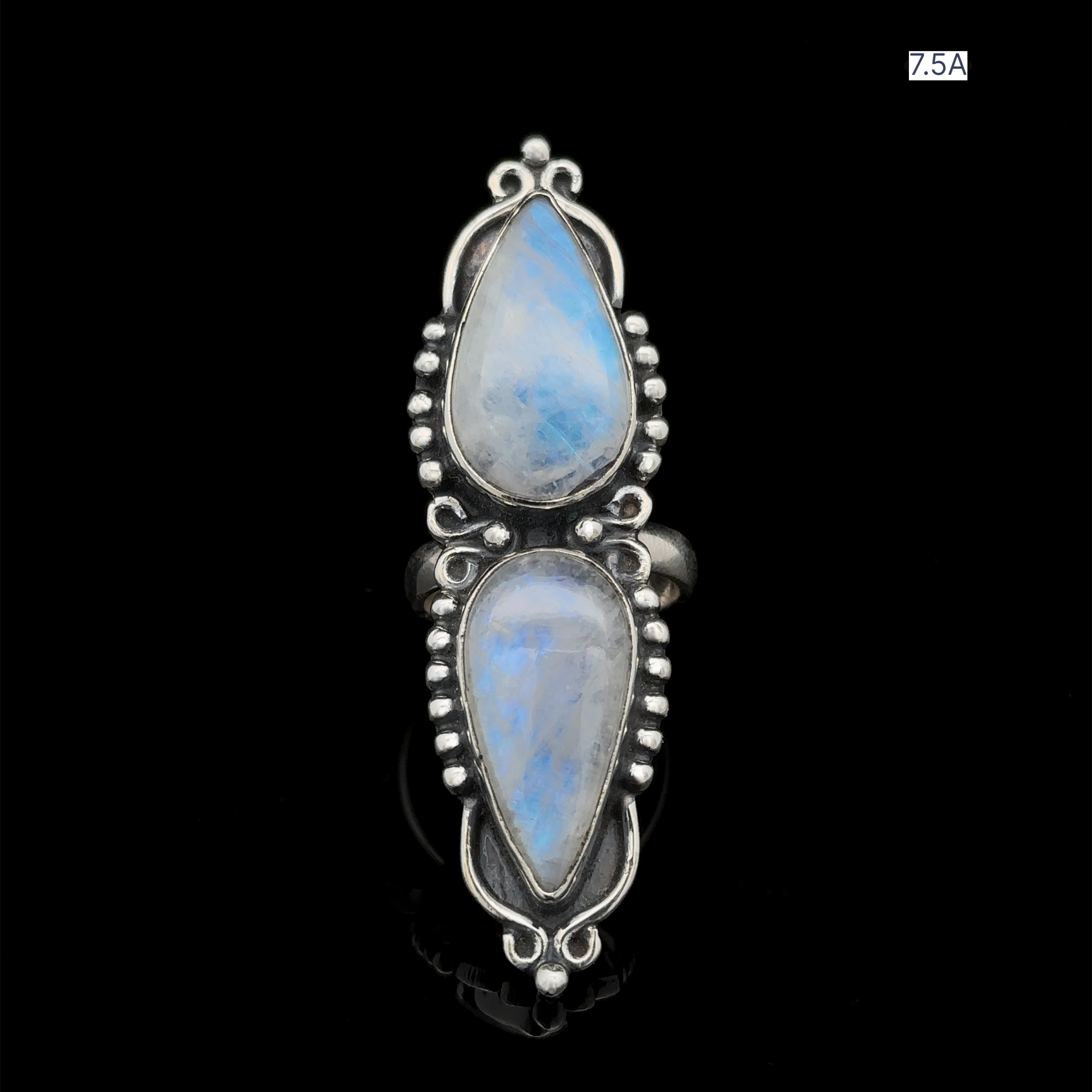 A sterling silver Long Double Teardrop Moonstone Ring featuring two teardrop-shaped moonstones with intricate designs and bead details, displayed on a black background. A small label in the upper right corner states "7.5A.
