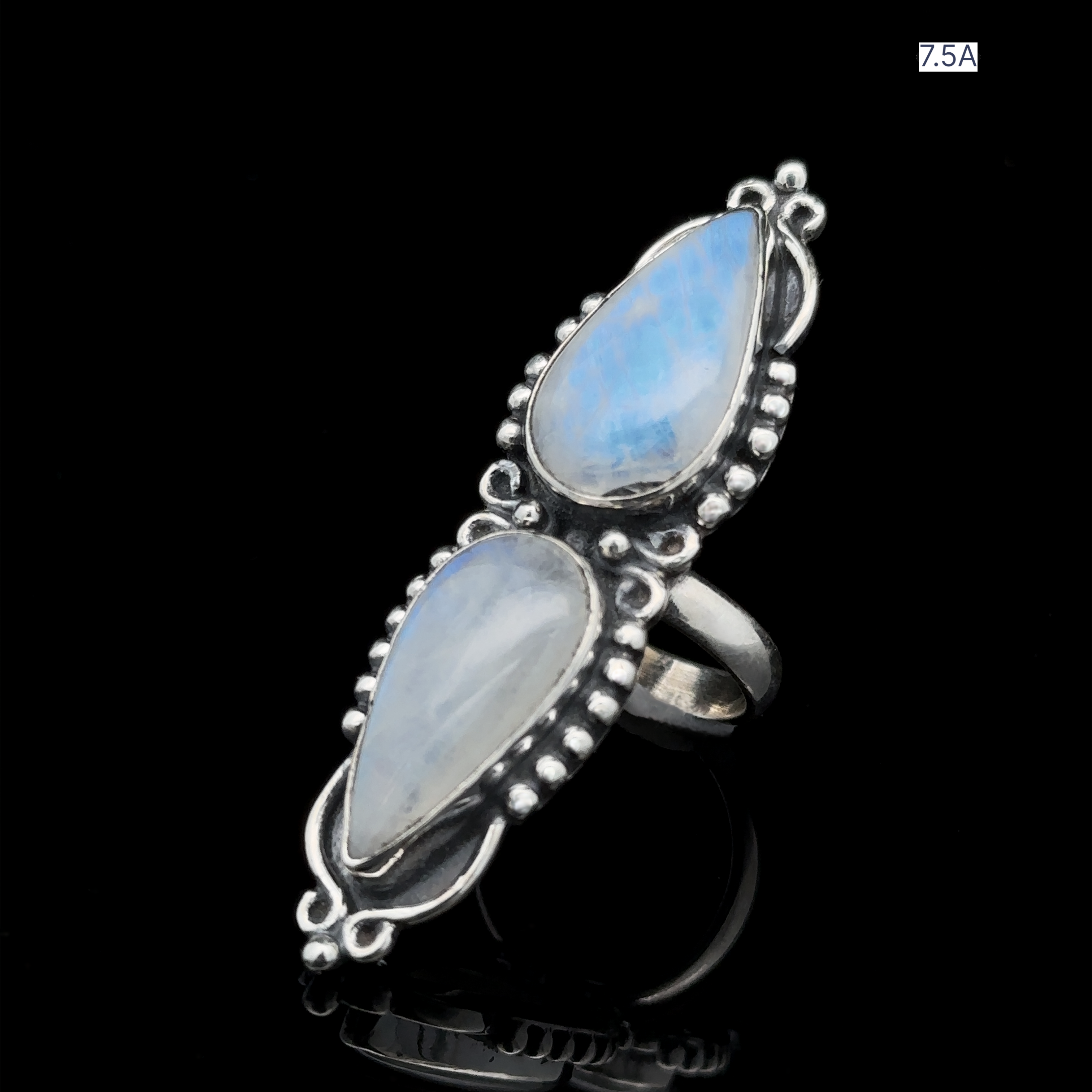 A Long Double Teardrop Moonstone Ring in sterling silver, showcasing two vertically positioned pear-shaped moonstones, encircled by small metal beads against a black background. A label in the corner reads "7.5A".