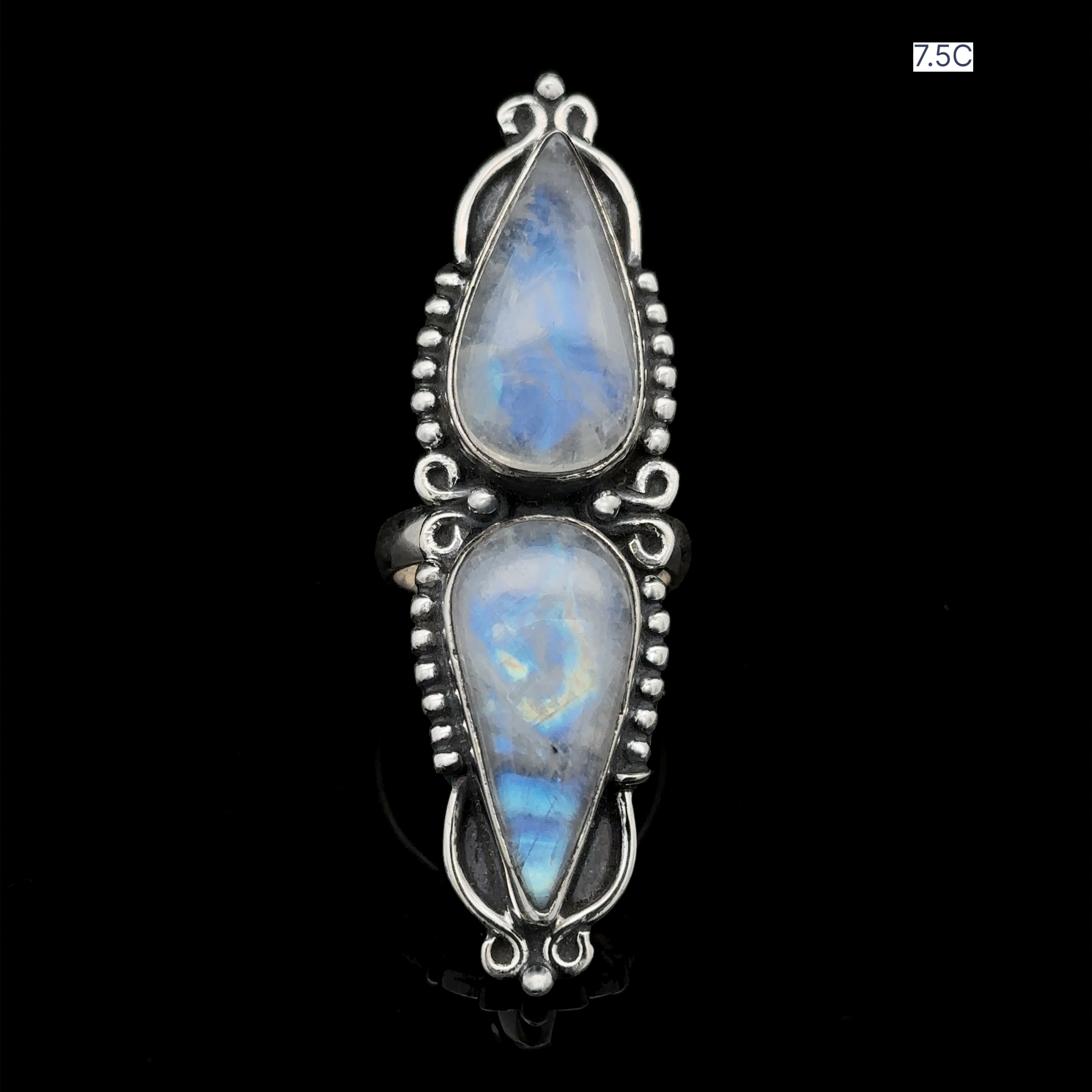 The Long Double Teardrop Moonstone Ring is a stunning statement piece featuring two vertically aligned teardrop-shaped moonstones, each bordered by intricate beadwork designs. The top moonstone is smaller than the bottom one, creating a captivating contrast. This sterling silver ring comes in size 7.5C.