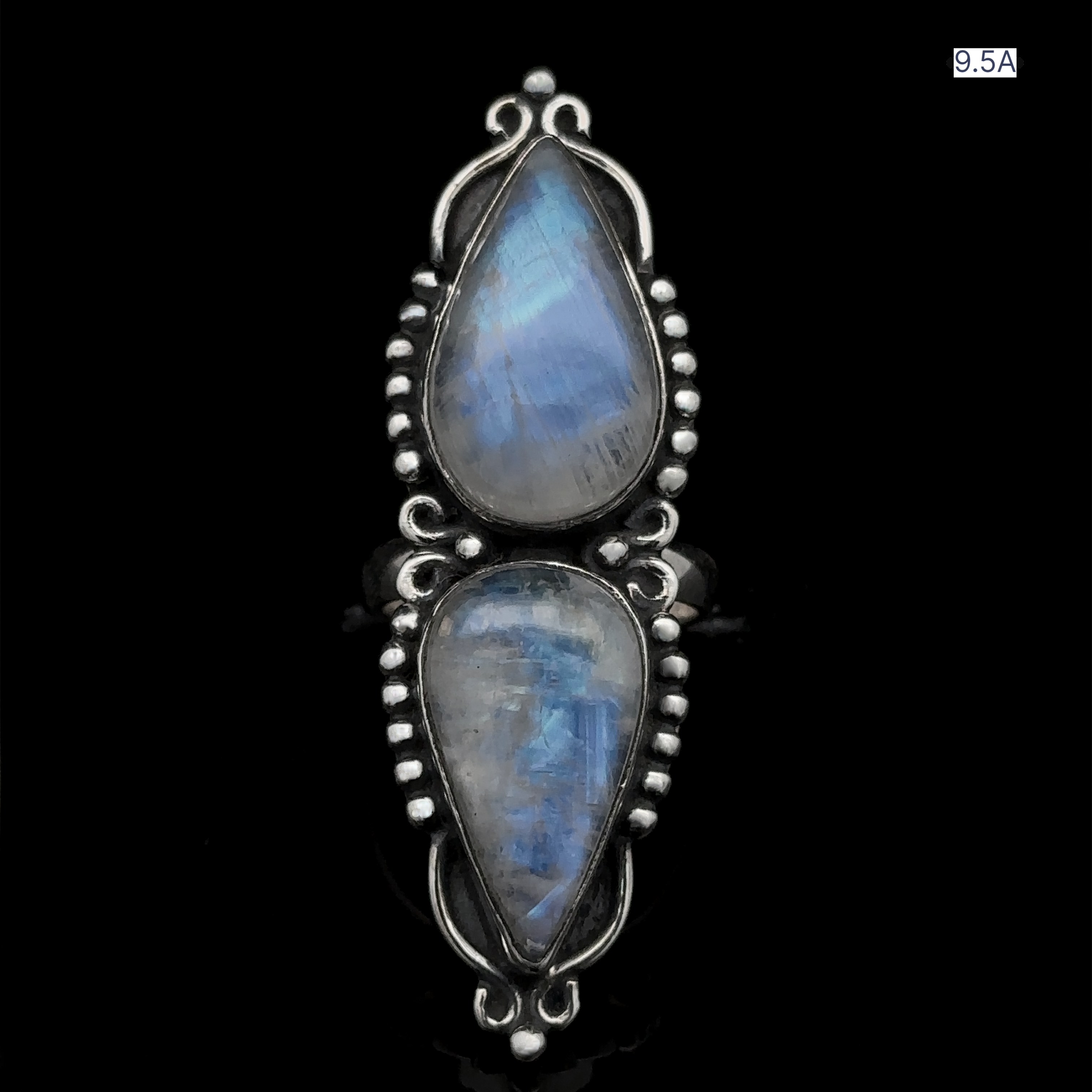 The Long Double Teardrop Moonstone Ring is a sterling silver piece showcasing two iridescent tear-shaped moonstones, one positioned above the other within a decorative bezel against a black backdrop. Additionally, this statement ring displays the number 9.5A at the top right corner.