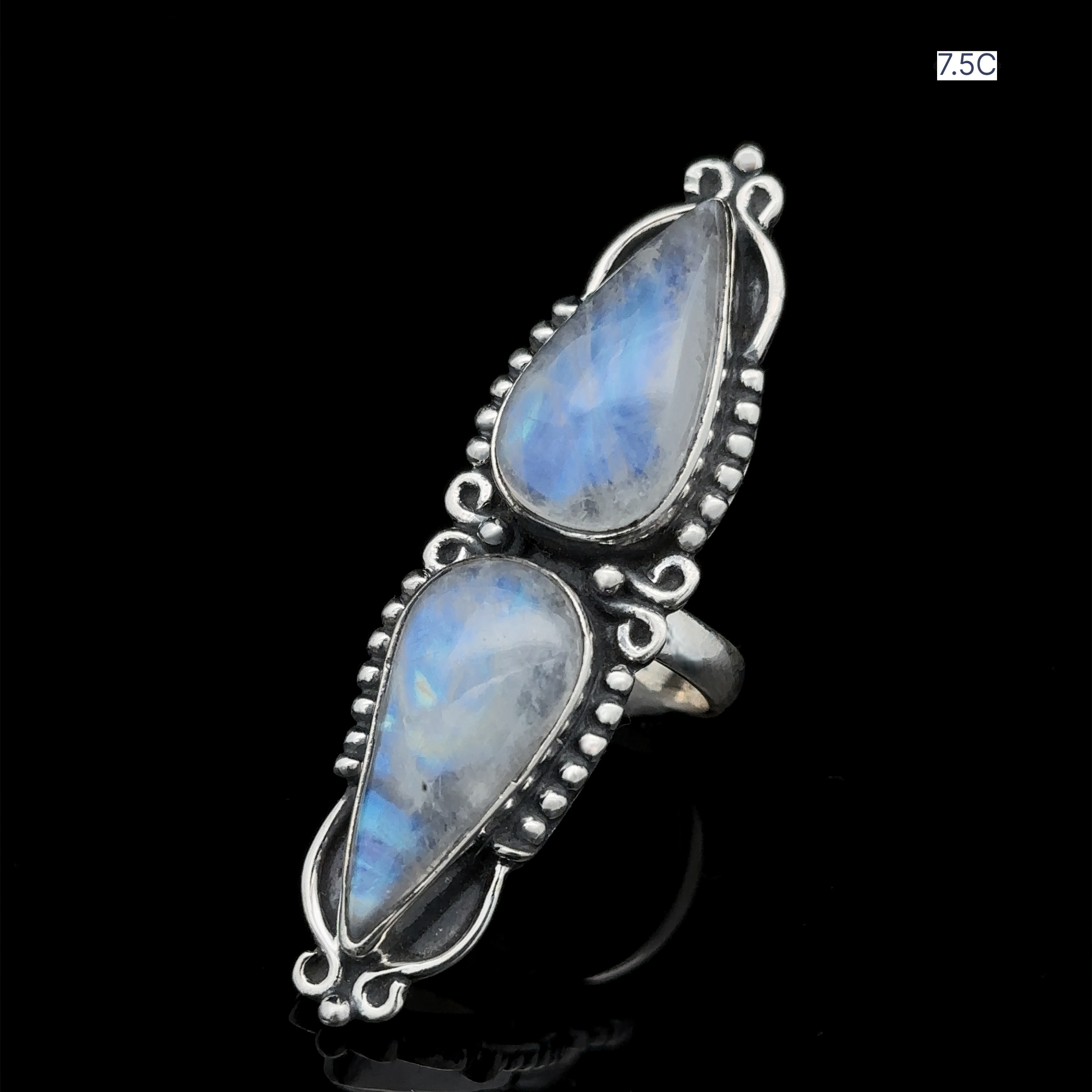 Introducing the Long Double Teardrop Moonstone Ring: a sterling silver statement piece featuring two vertically-set teardrop-shaped blue moonstones, adorned with intricate bead detailing against a striking black background. This elegant and charming ring is sure to elevate any ensemble.