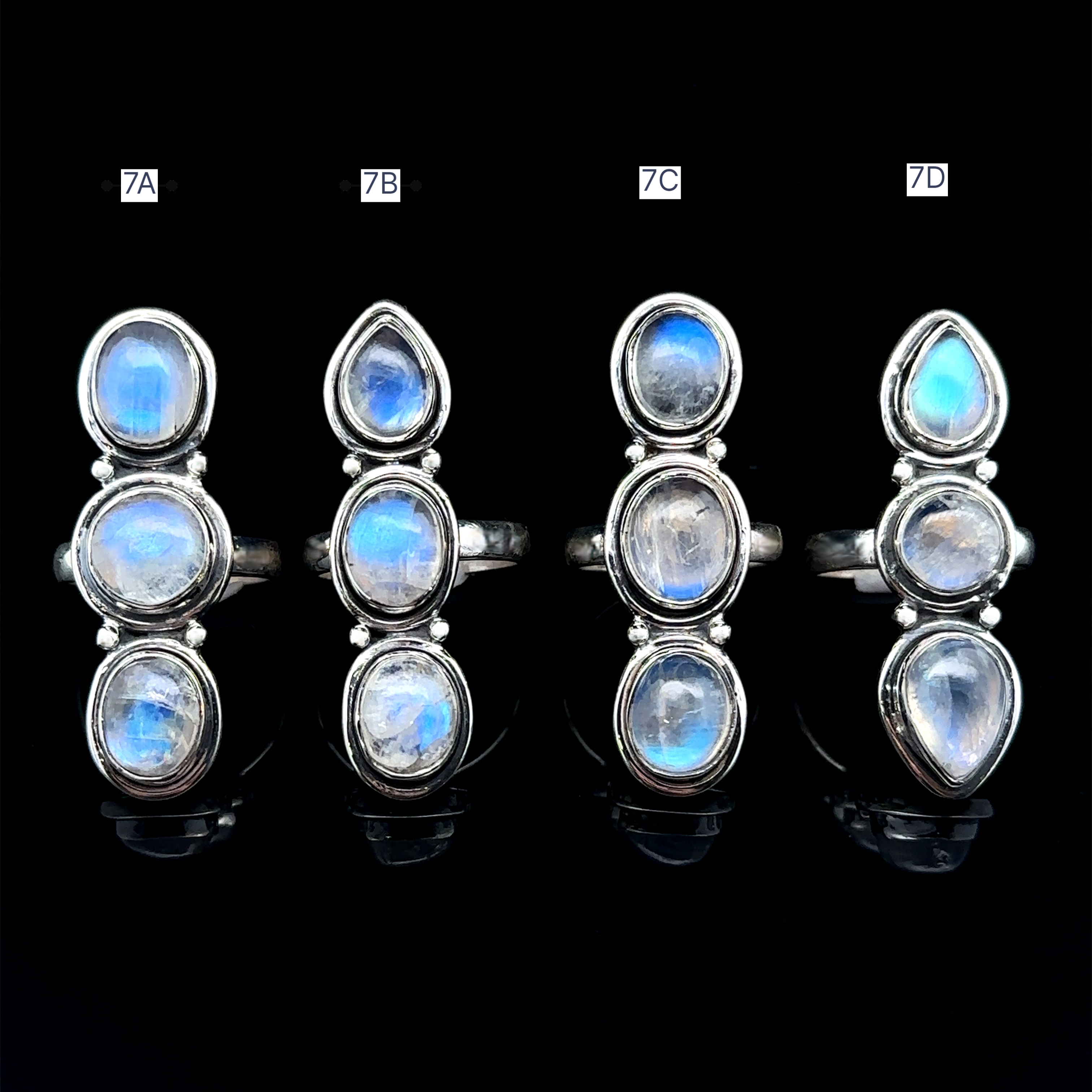 Against a black background, four Triple Moonstone Rings are displayed vertically, each adorned with three oval moonstones. Labeled as 7A, 7B, 7C, and 7D, these sterling silver rings embody the mystical allure of goddess energy.