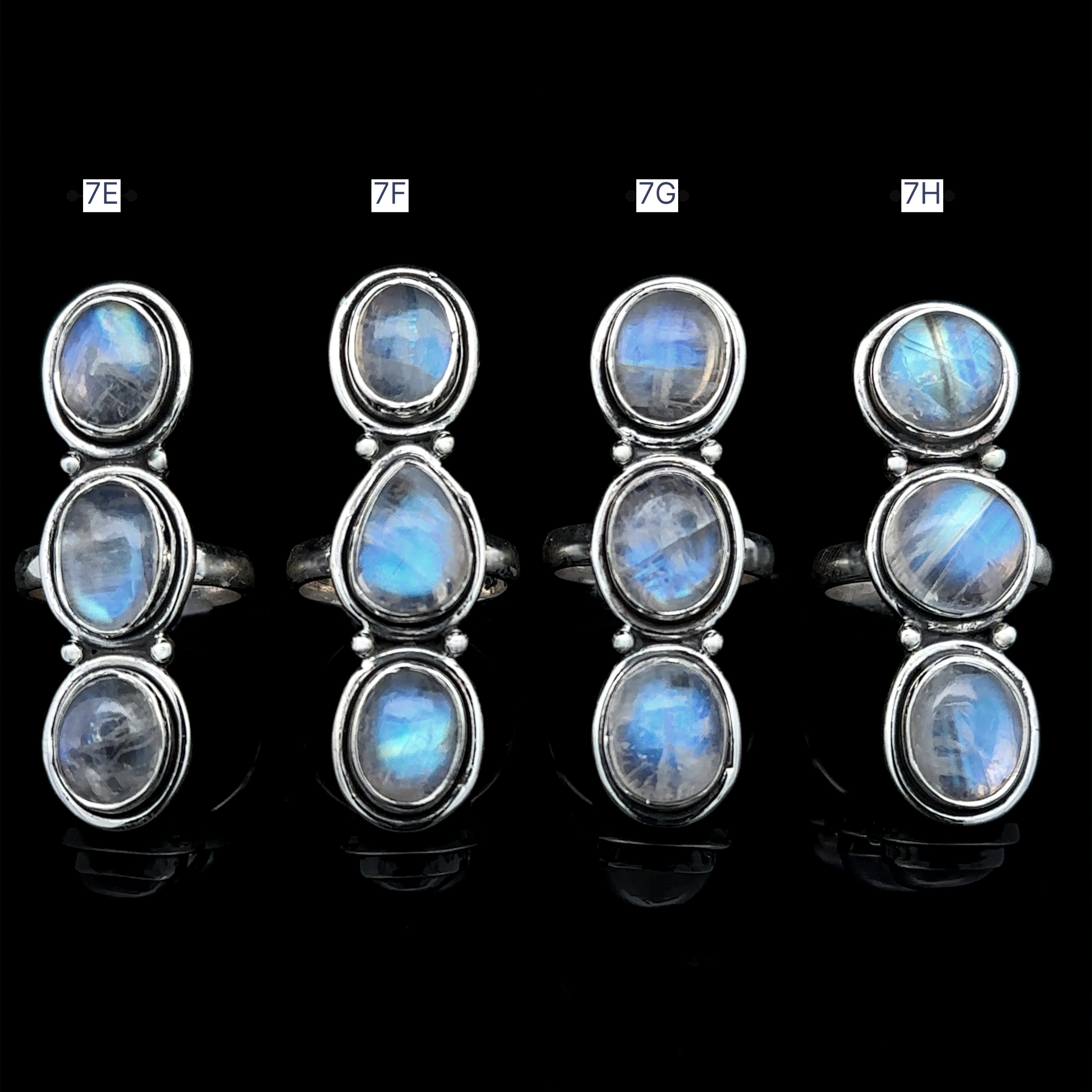 Four Triple Moonstone Rings crafted from sterling silver, featuring oval blue gemstones with unique arrangements of three stones. Each ring is labeled 7E, 7F, 7G, and 7H. A black background enhances their shine, radiating a captivating goddess energy.