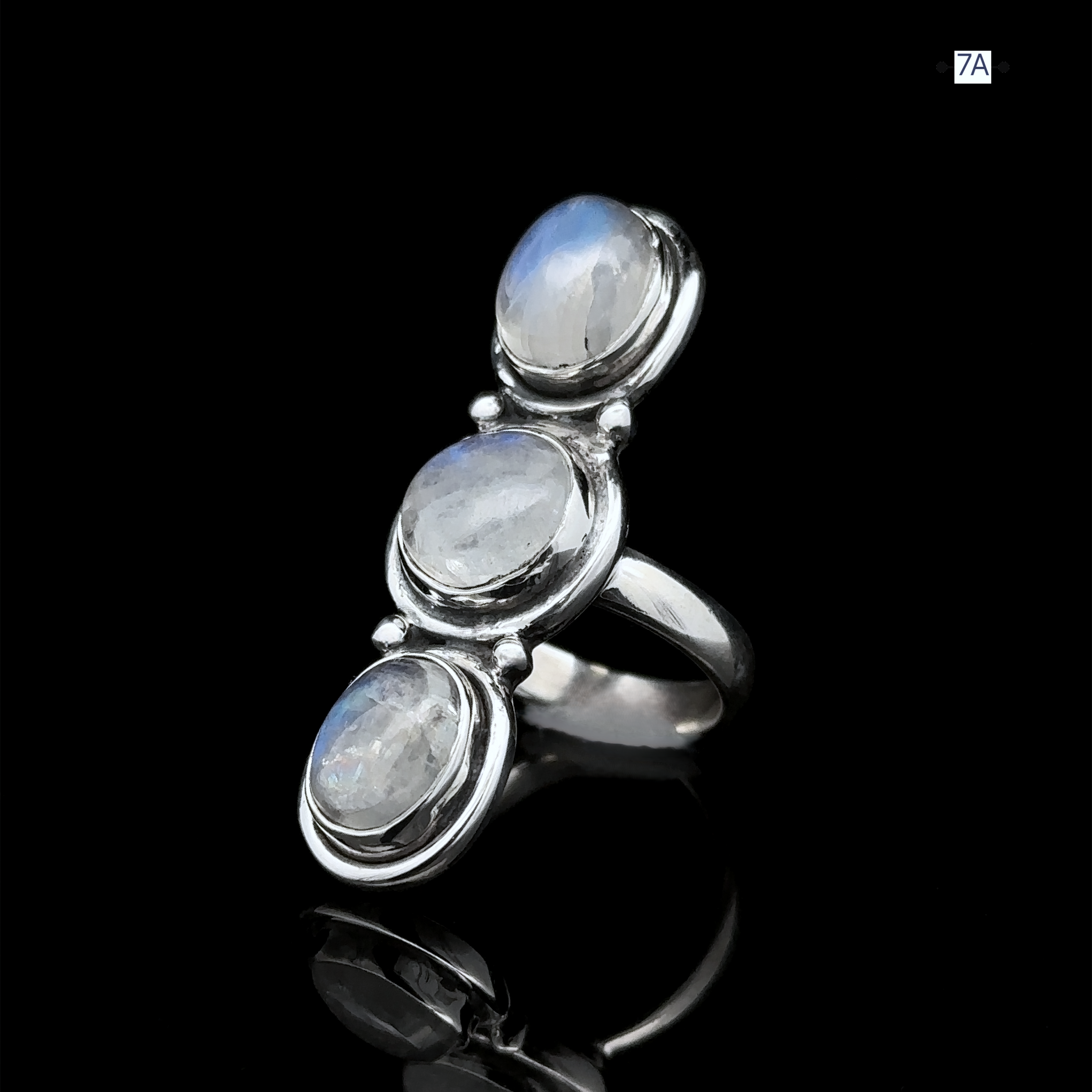 The Triple Moonstone Ring, crafted from sterling silver, showcases three round moonstone gemstones arranged vertically against a black backdrop. This exquisite piece exudes a goddess-like energy with its ethereal glow.