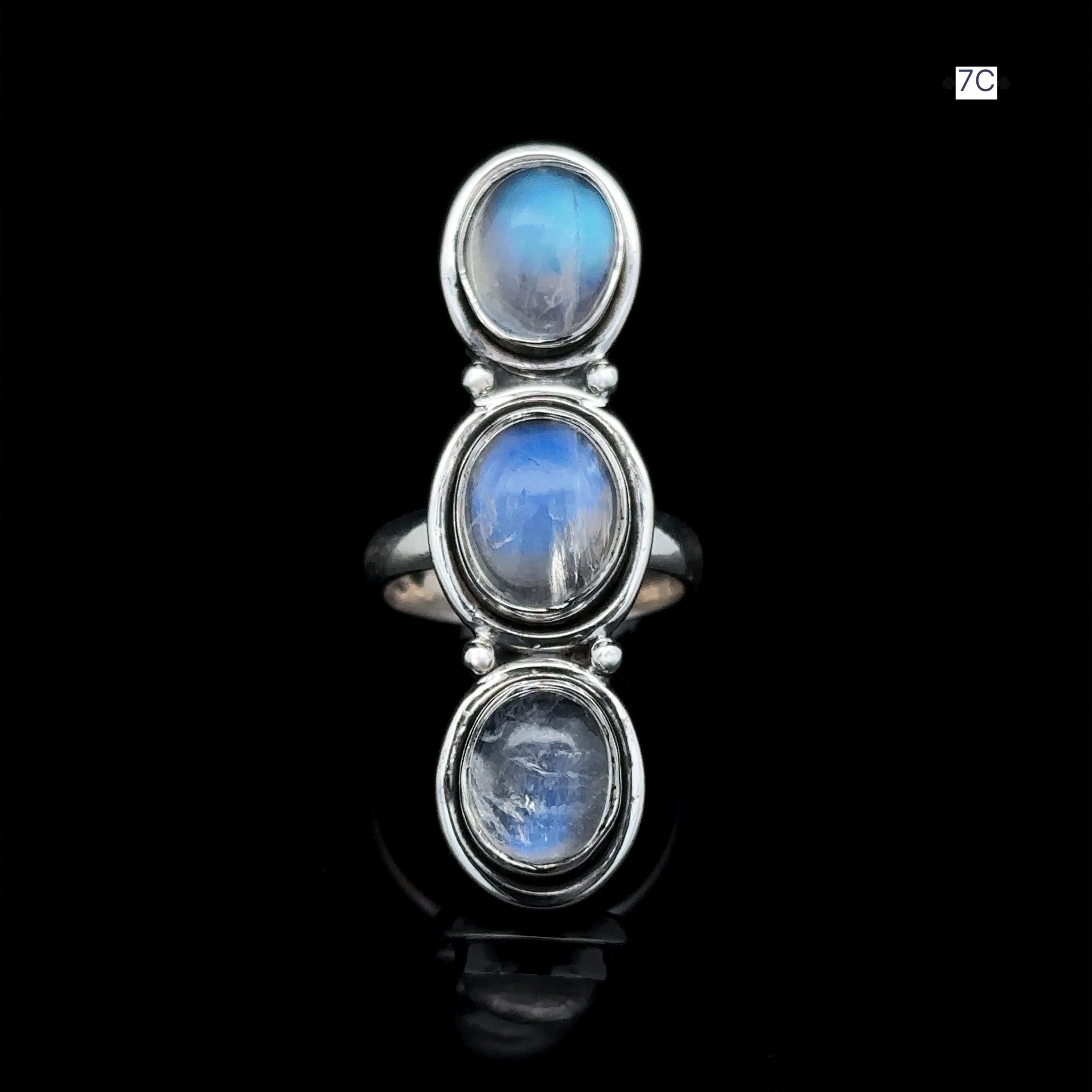 The Triple Moonstone Ring features three oval moonstone gems set vertically against a striking black background, exuding a radiant goddess energy.