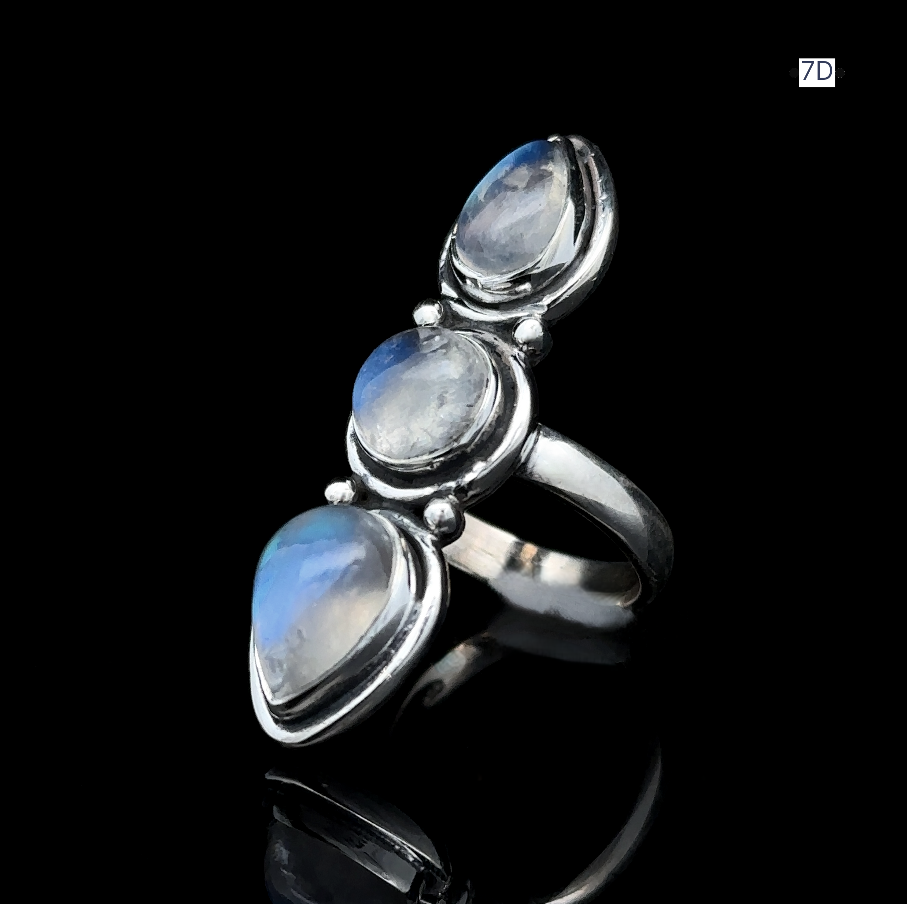 The Triple Moonstone Ring, made of sterling silver and featuring three round, iridescent gemstones set against a black background, exudes goddess energy.