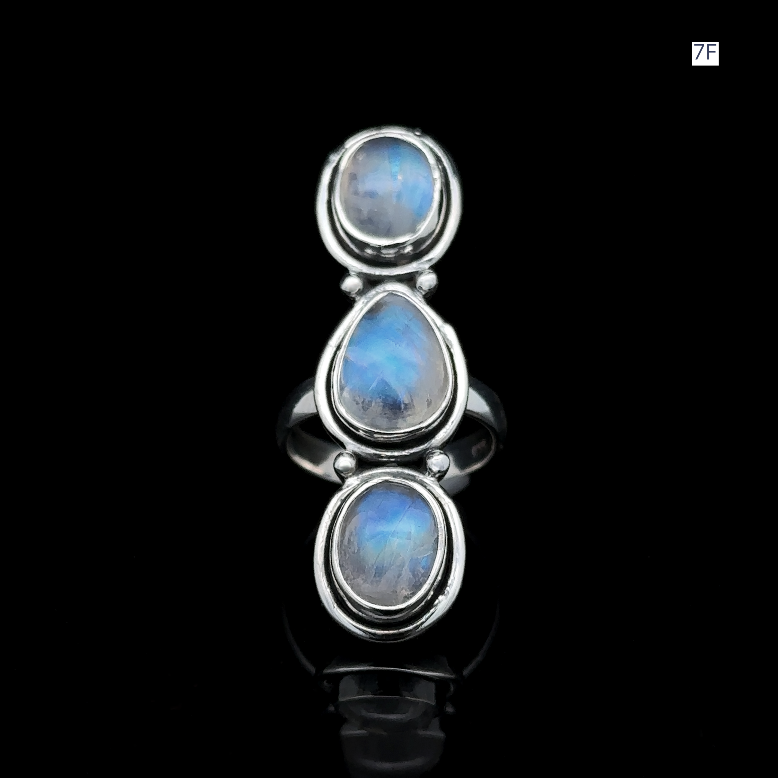 The Triple Moonstone Ring features three oval blue gemstones set vertically against a striking black background, radiating goddess energy.