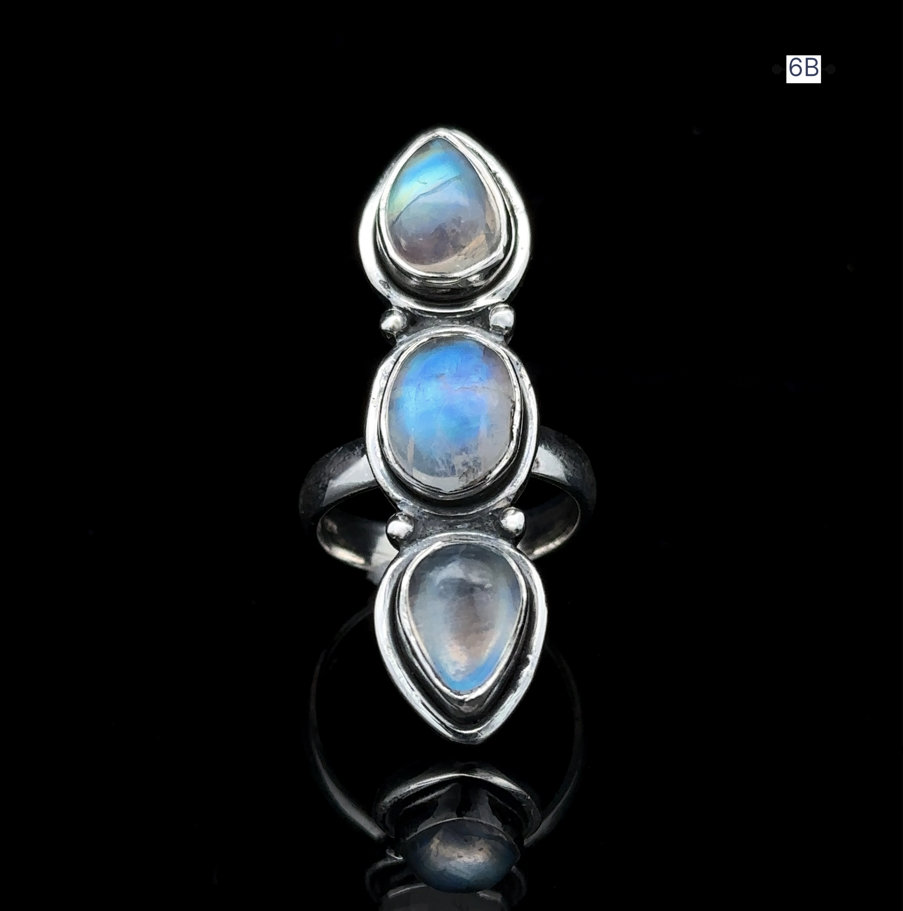 The Triple Moonstone Ring showcases three vertically aligned teardrop-shaped blue moonstones set in sterling silver, radiating a goddess-like aura against its dark backdrop.