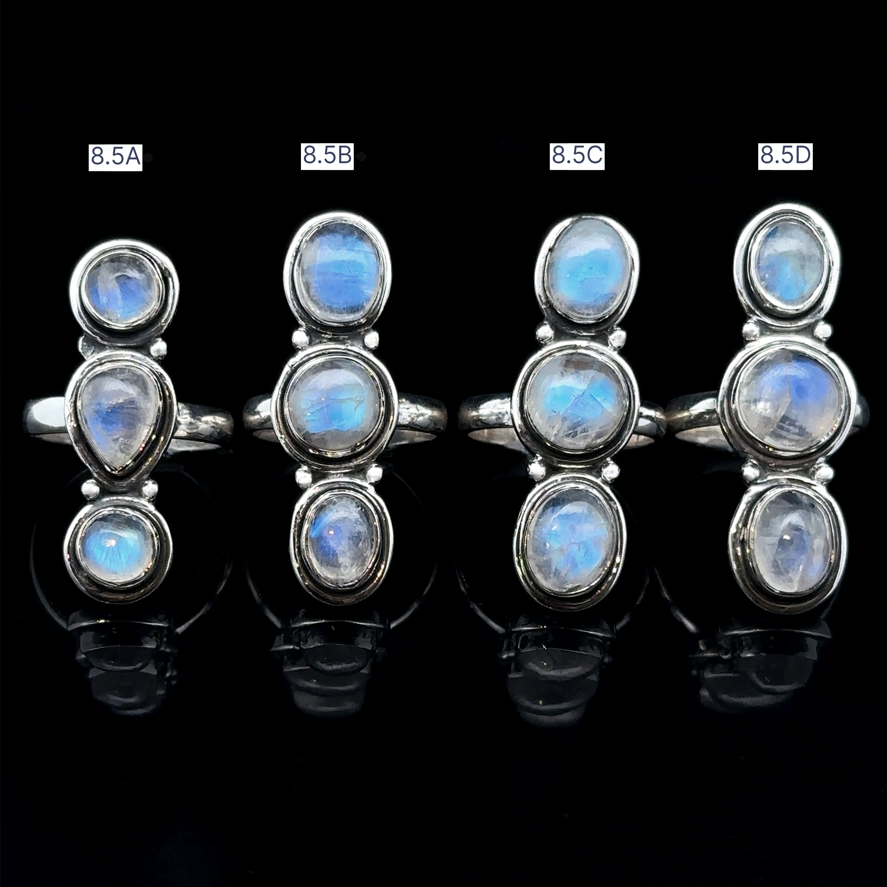 Four sterling silver rings adorned with oval moonstones exude goddess energy, beautifully showcased on a black background. Each exquisite Triple Moonstone Ring is marked as 8.5A, 8.5B, 8.5C, and 8.5D.