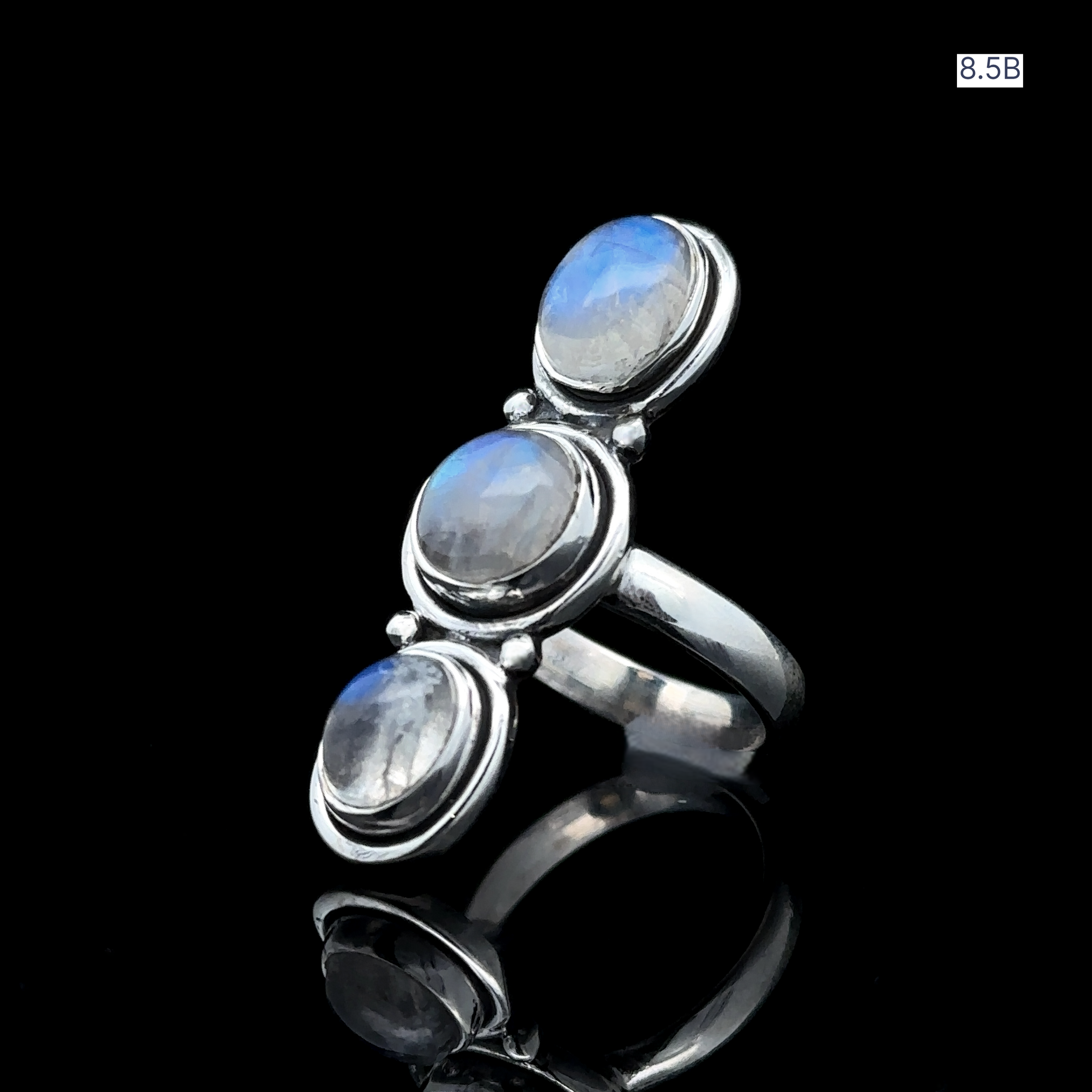 The Triple Moonstone Ring showcases three vertically aligned round gemstones, channeling goddess energy. It is crafted from sterling silver and has a discreet size label "8.5B" in the corner.