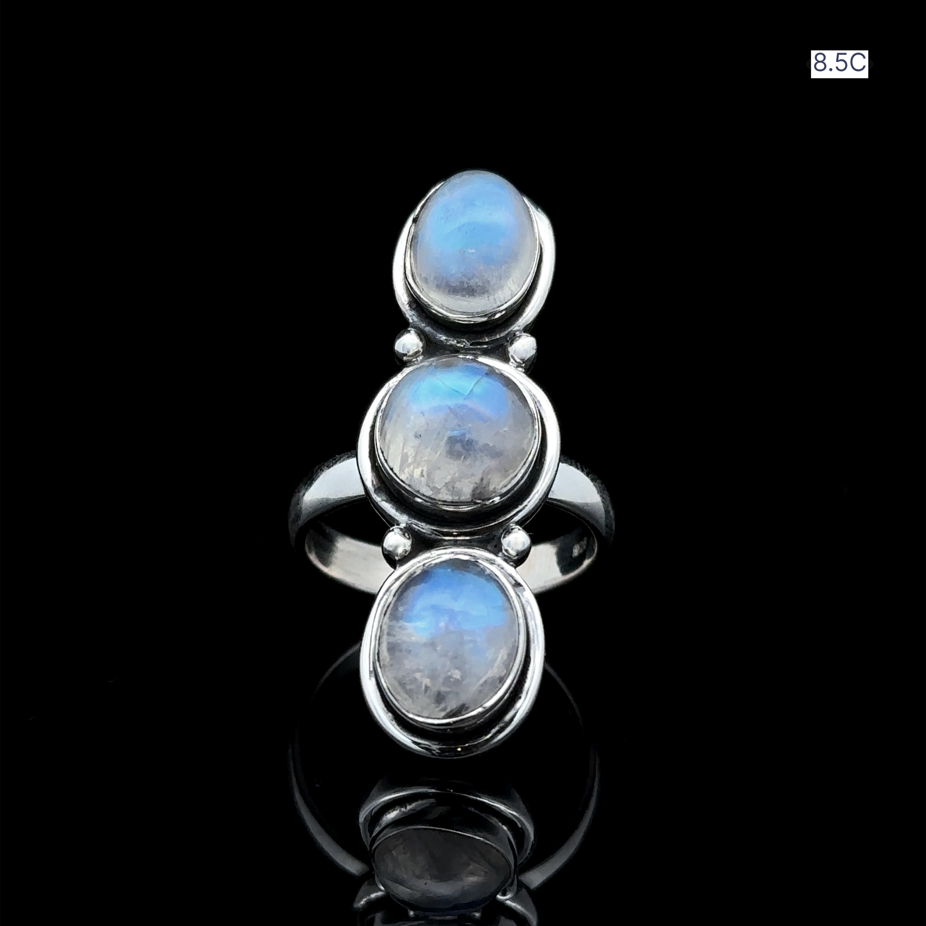 The Triple Moonstone Ring, crafted from sterling silver and featuring three captivating oval moonstone gems, evokes goddess energy as it elegantly rests on a black reflective surface.