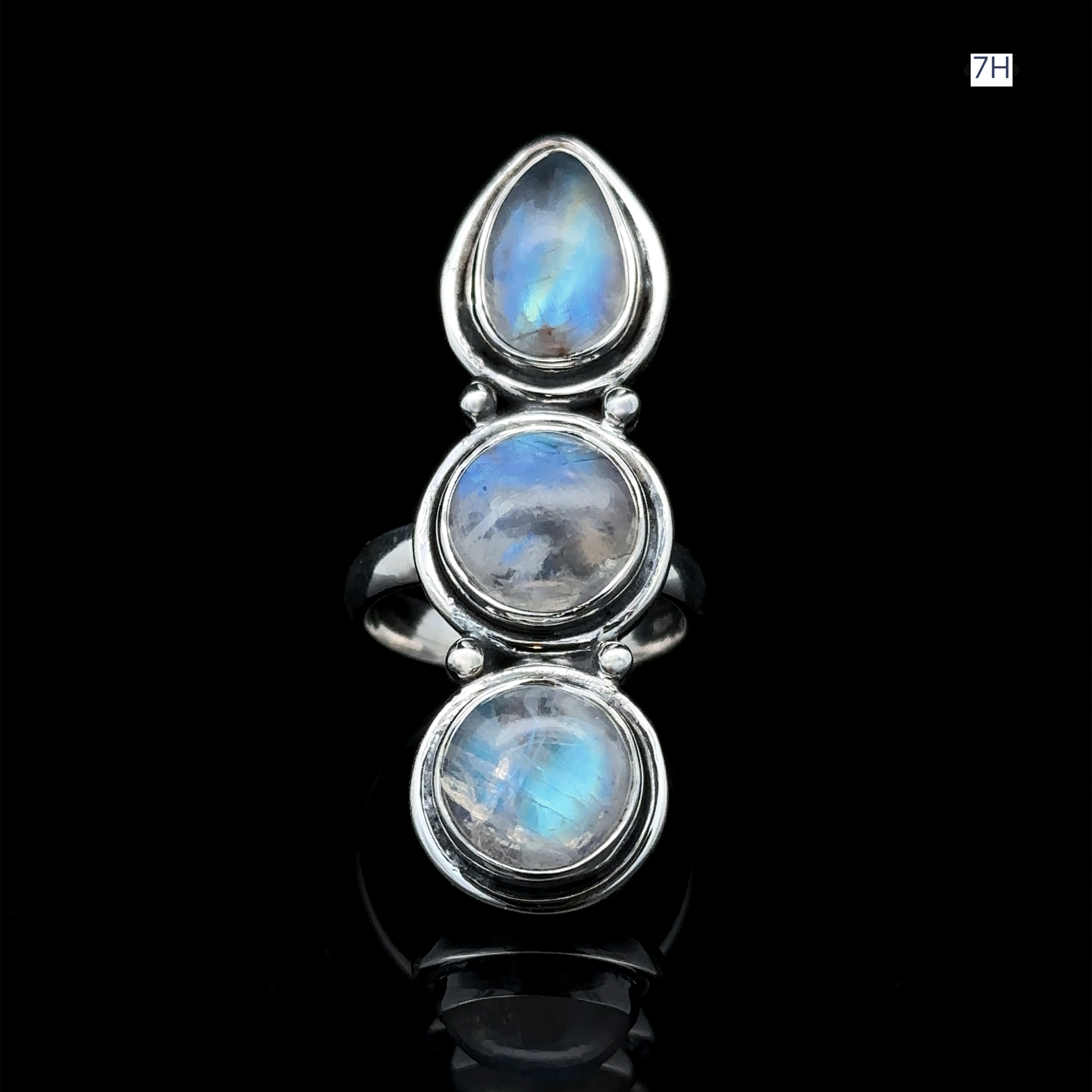 The Triple Moonstone Ring, crafted from sterling silver, features a teardrop-shaped moonstone on top with two smaller round stones beneath, exuding goddess energy. Set against a black background, its ethereal allure is truly captivating.