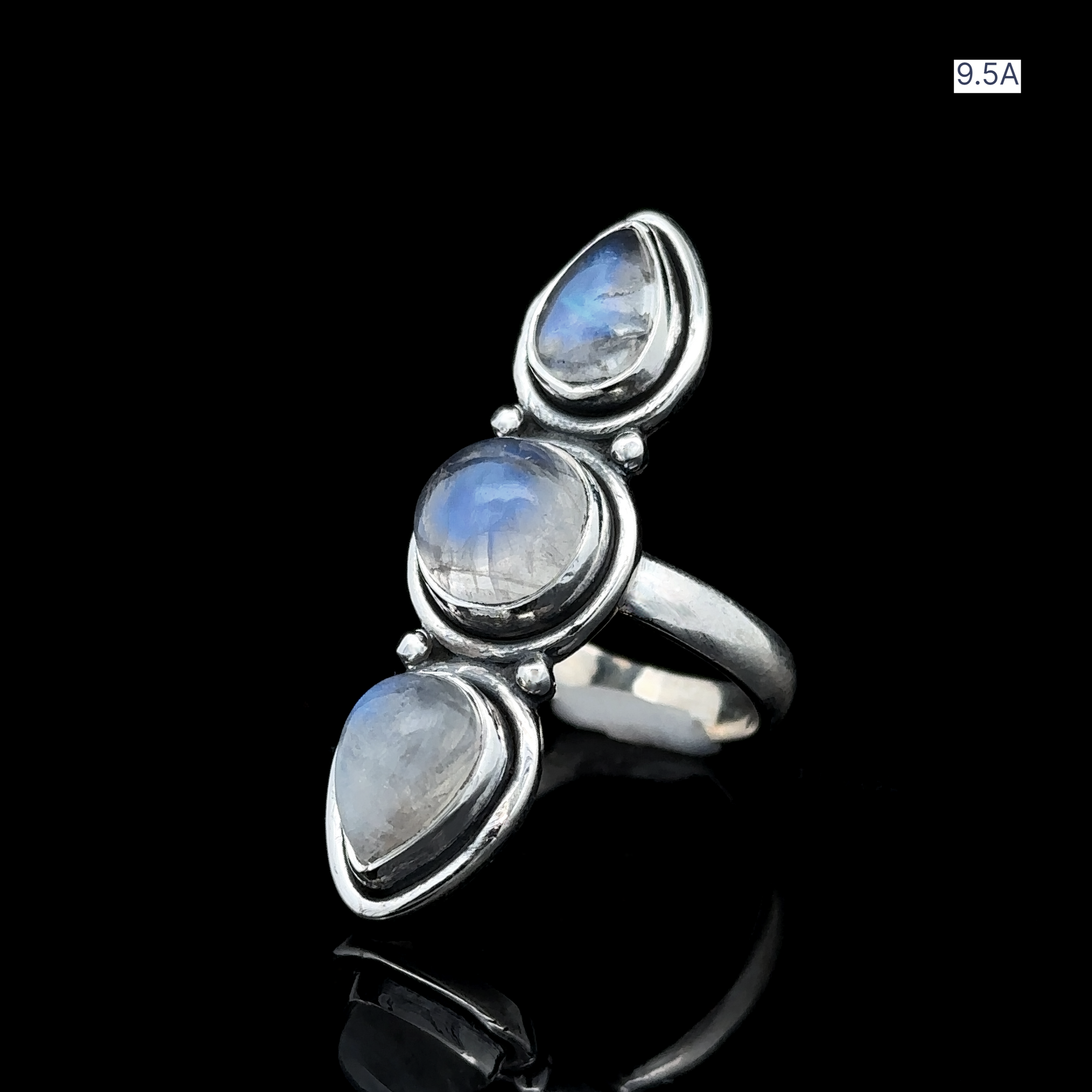 The Triple Moonstone Ring is made from sterling silver and showcases three vertically set teardrop-shaped moonstones against a black background, emanating goddess energy. It is available in size 9.5A.