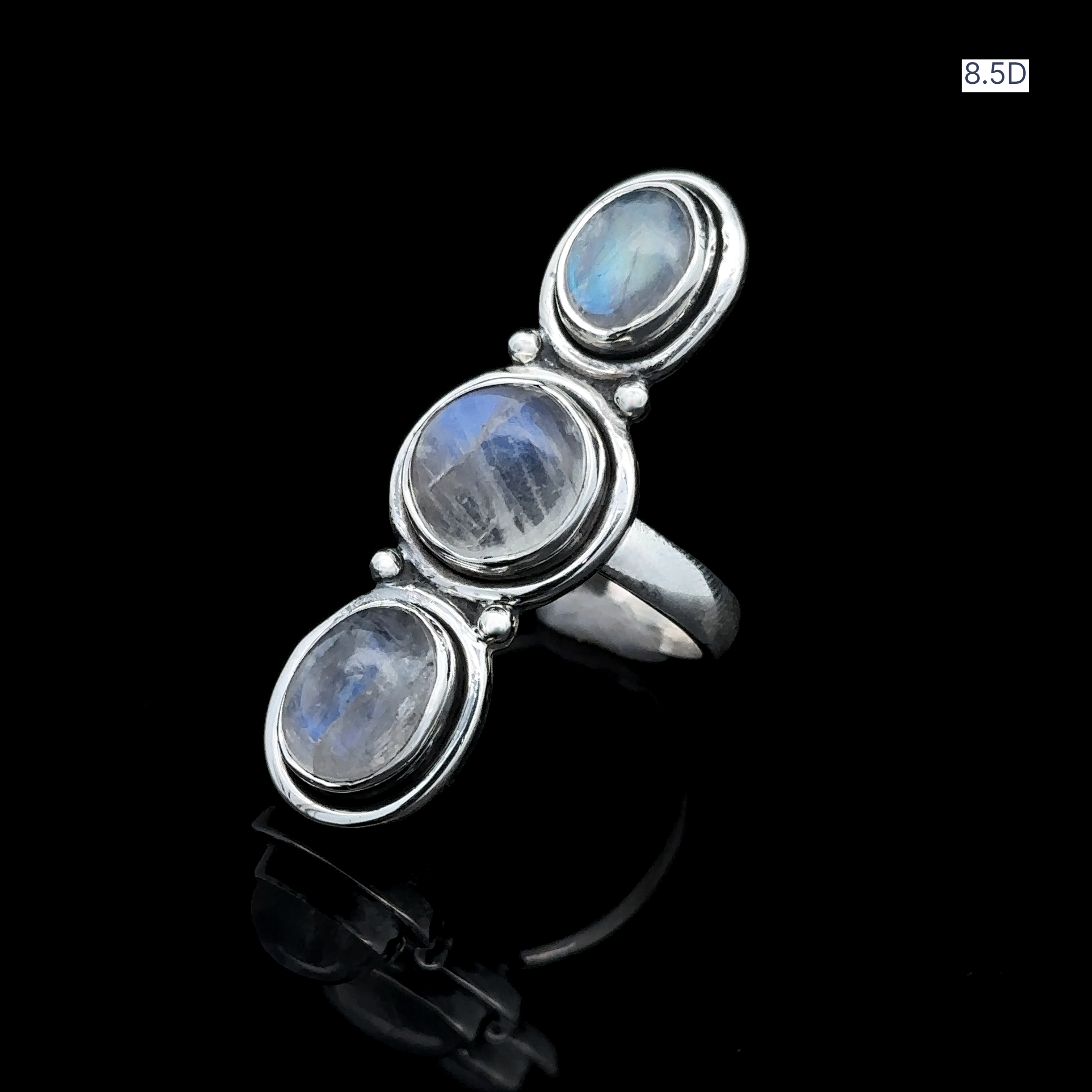 The Triple Moonstone Ring exudes goddess energy with its stunning design, featuring three vertically set oval moonstones in sterling silver, beautifully displayed on a reflective black surface.