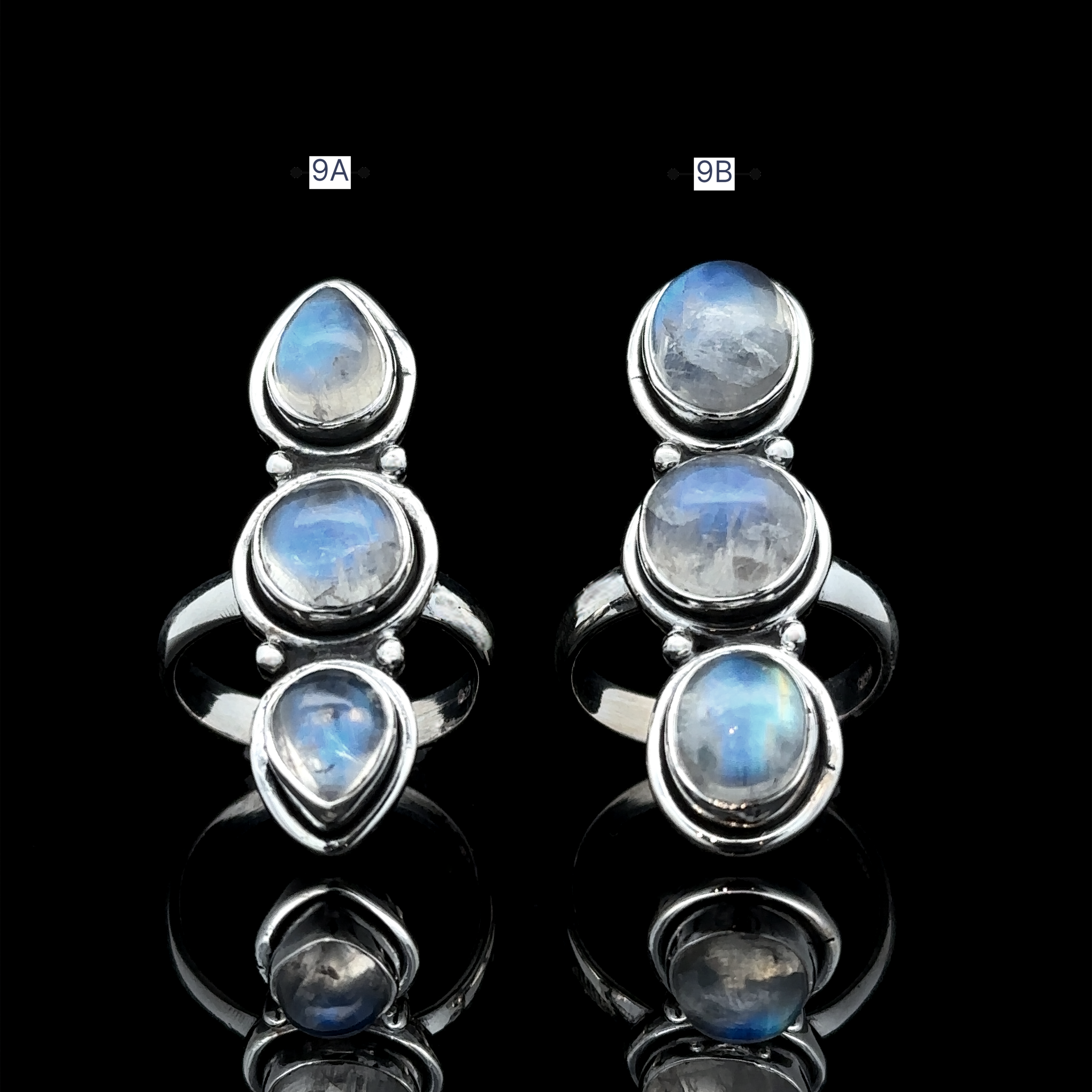 Two sterling silver rings featuring moonstone gems are showcased on a reflective black surface. The Triple Moonstone Ring, identified as Ring 9A, embodies goddess energy with three teardrop-shaped stones. Meanwhile, Ring 9B elegantly highlights one round and two teardrop-shaped stones.