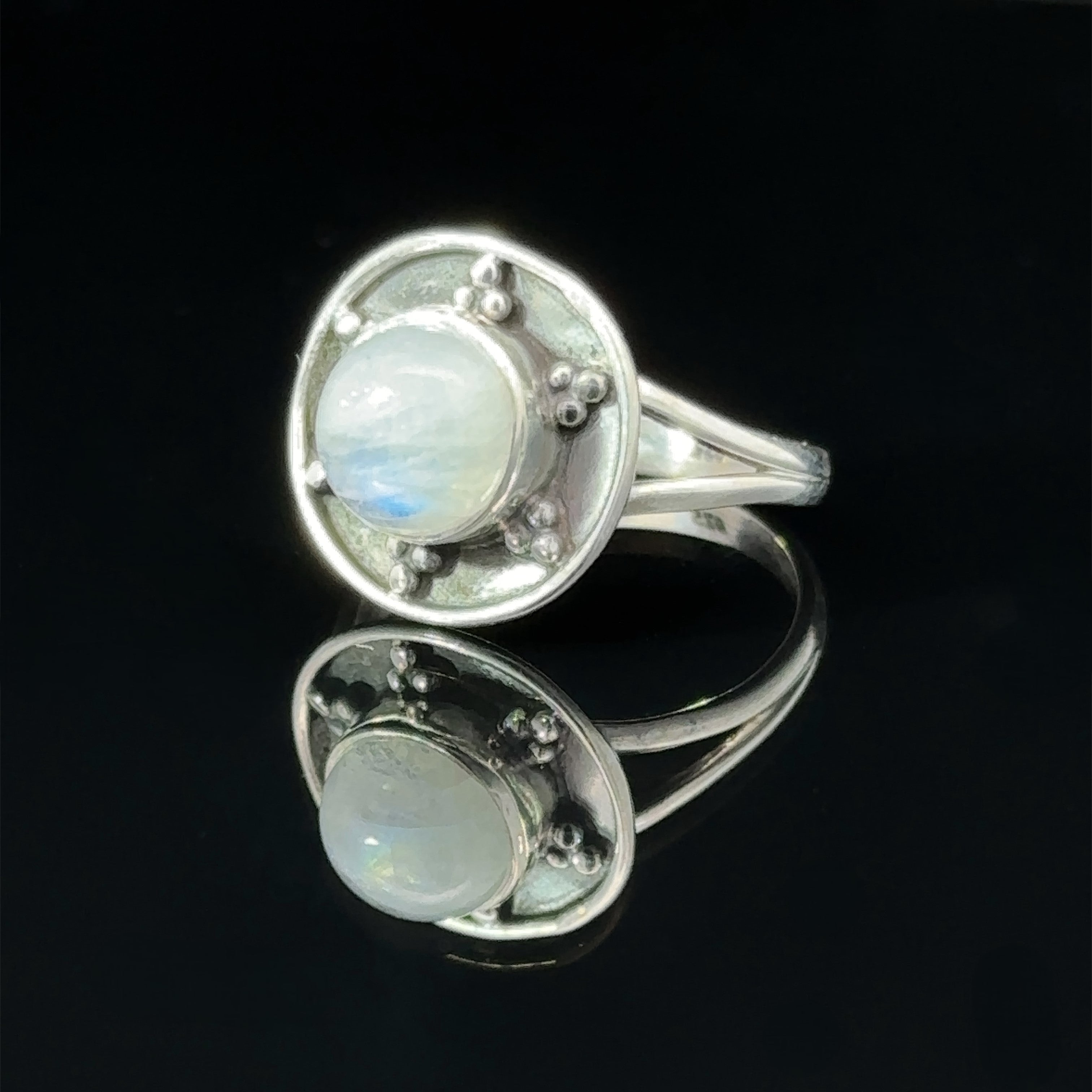 A Gemstone Ring With Unique Oxidized Design featuring a round moonstone set in a circular design with decorative elements, displayed against a black background.