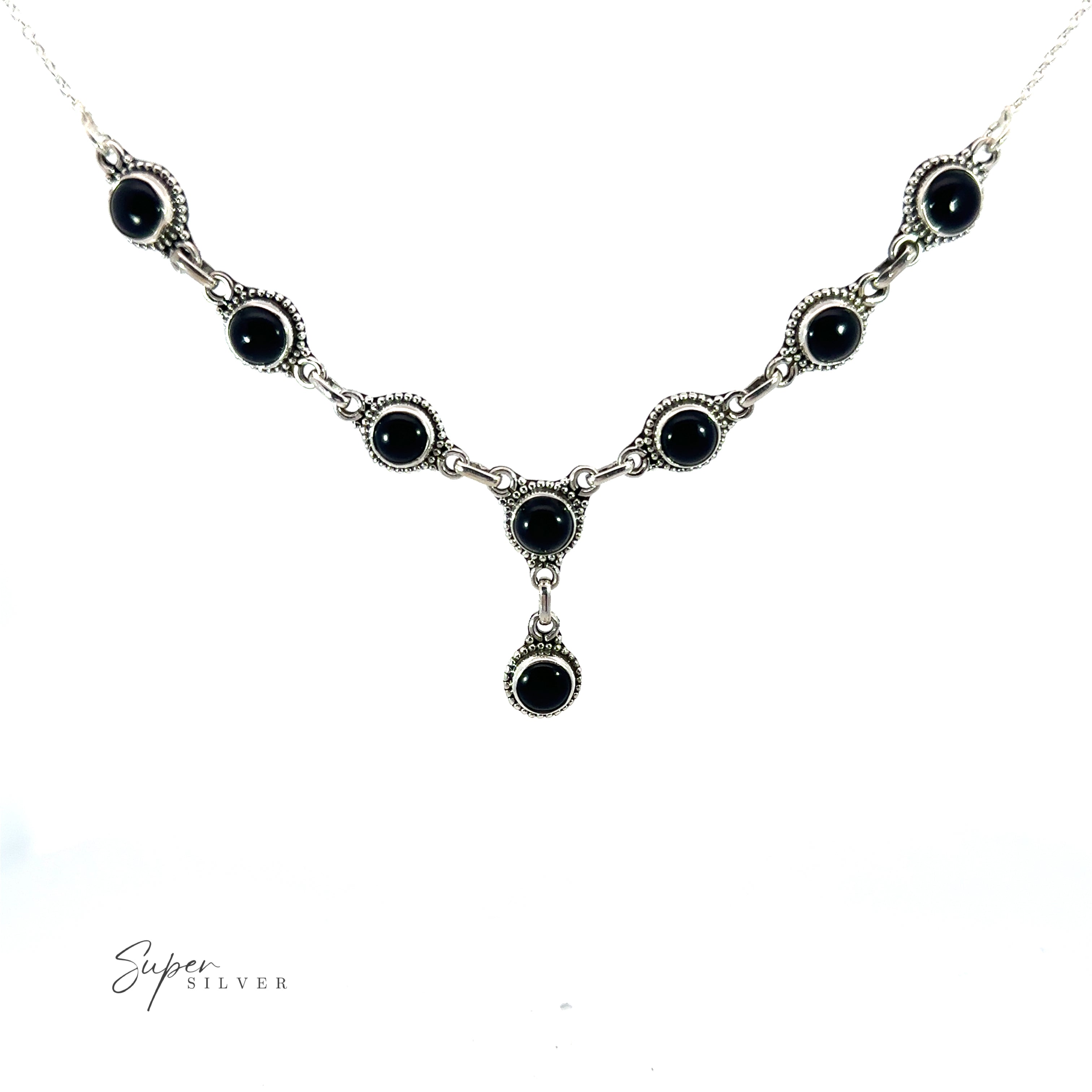 This Round Gemstone Y Necklace with Ball Border features interconnected circular black stones on a white background, epitomizing bohemian style jewelry. The Round Gemstone Y Necklace with Ball Border design is completed with a dangling pendant that showcases an additional black stone at the bottom center.
