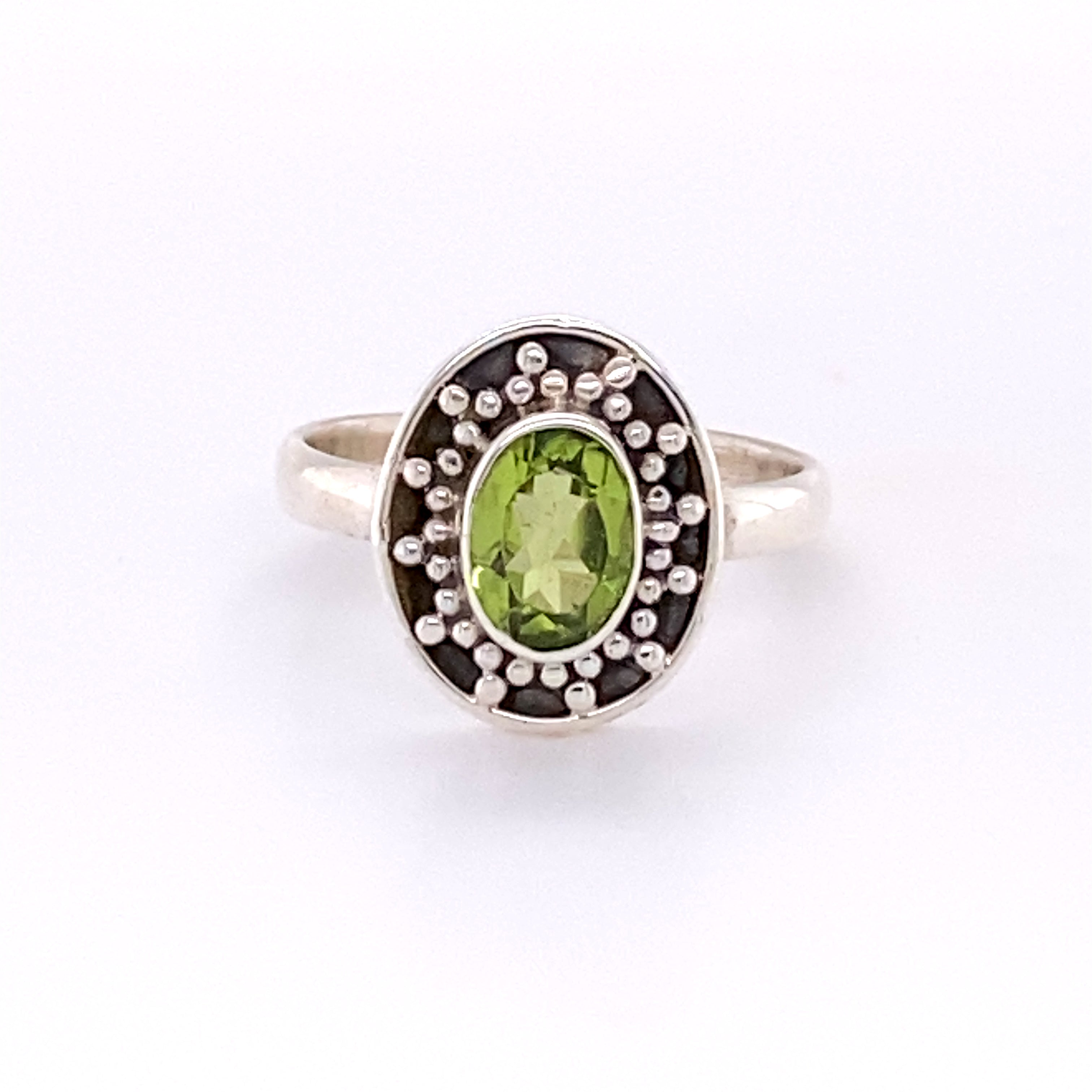 The Oval Peridot Dotted Shield Ring featuring an oval green gemstone surrounded by decorative Bali-styled disk setting and intricate silver beadwork.