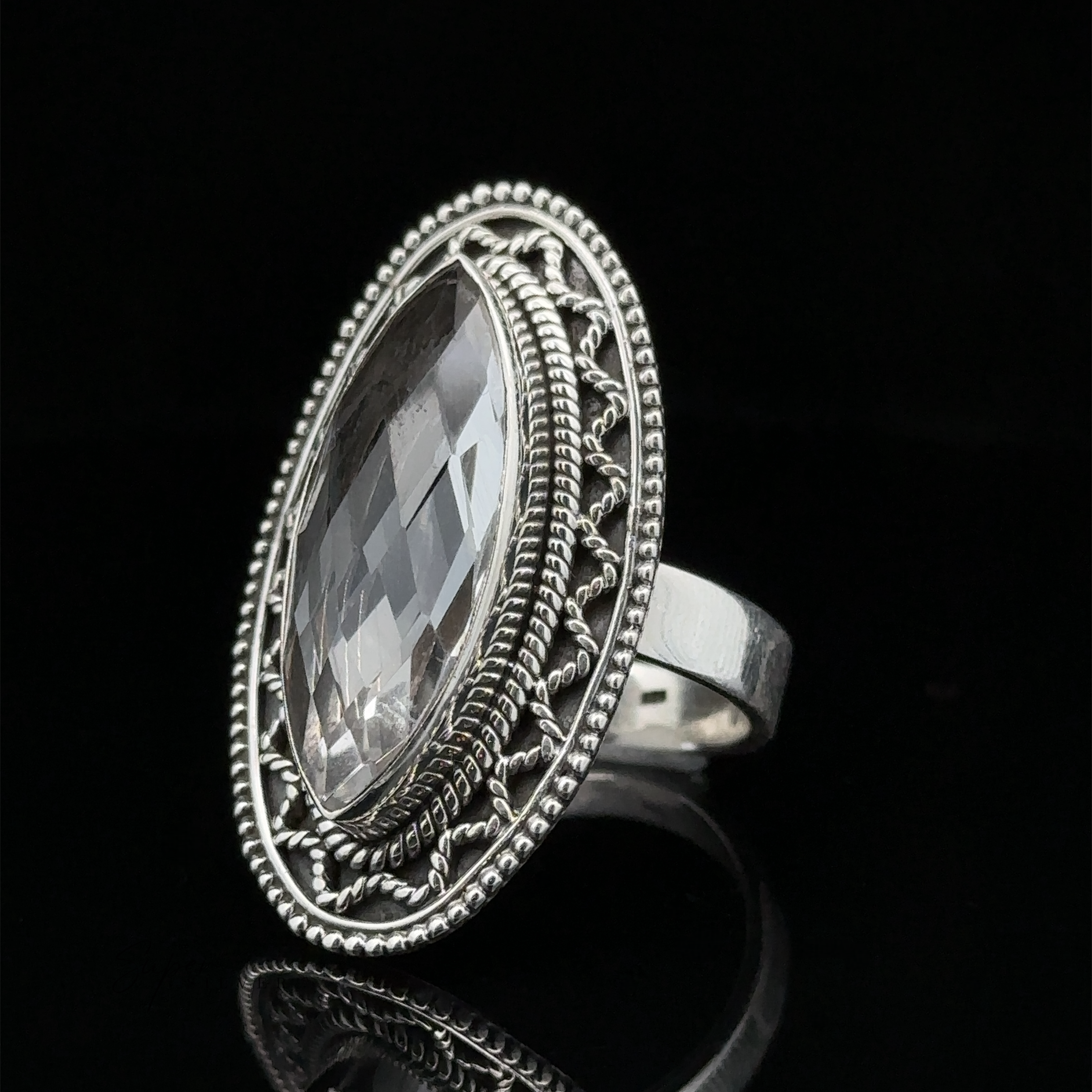 A Bohemian twist on elegance, this Marquise Shaped Gemstone Ring With Vintage Shield Border features an oval-shaped, faceted clear gemstone set in an ornate bezel against a black background.