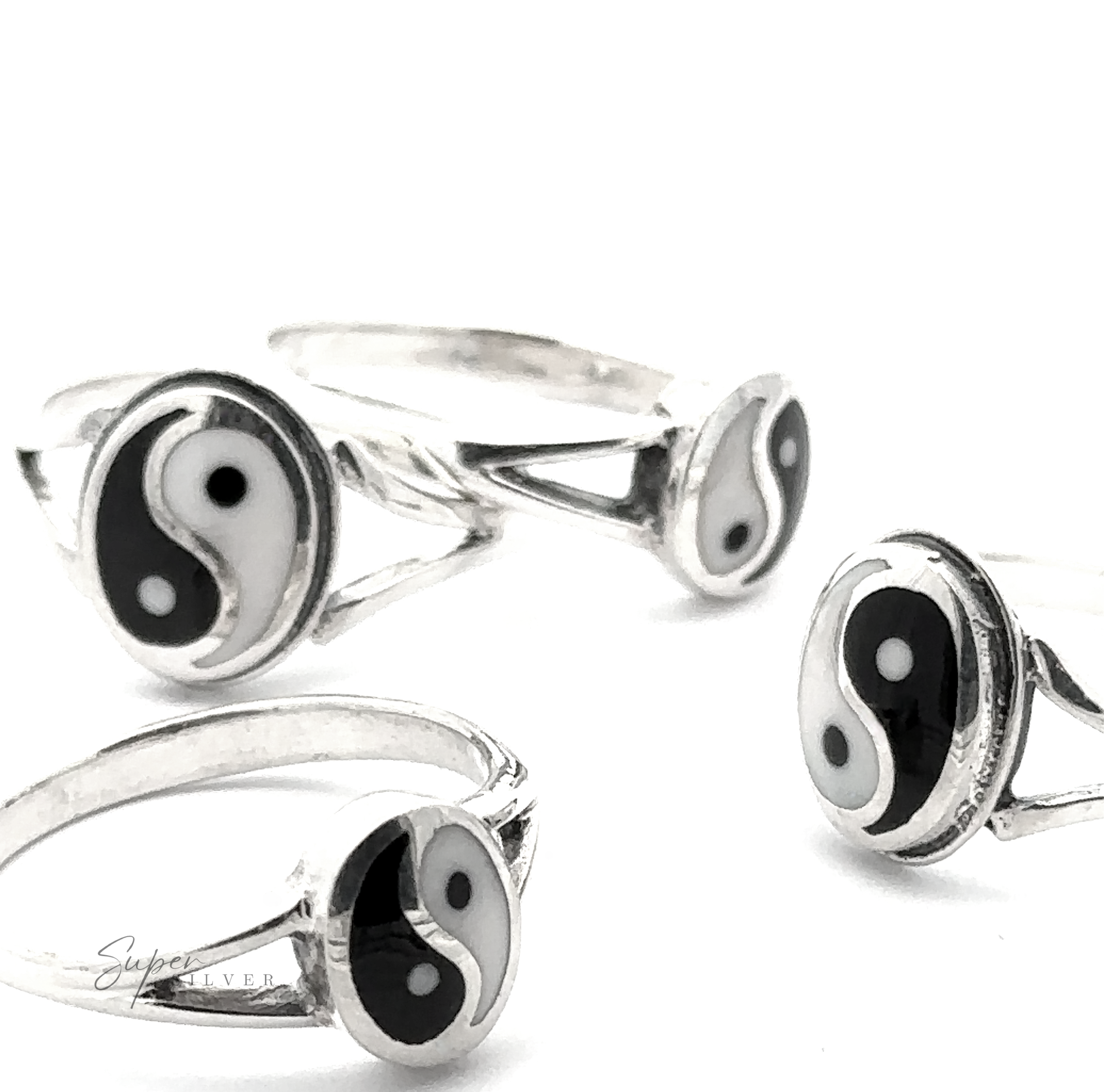 Four Simple Inlaid Yin-Yang Rings, crafted from sterling silver and featuring black and white yin-yang symbols, are artfully scattered on a white background, showcasing minimalist jewelry at its finest.