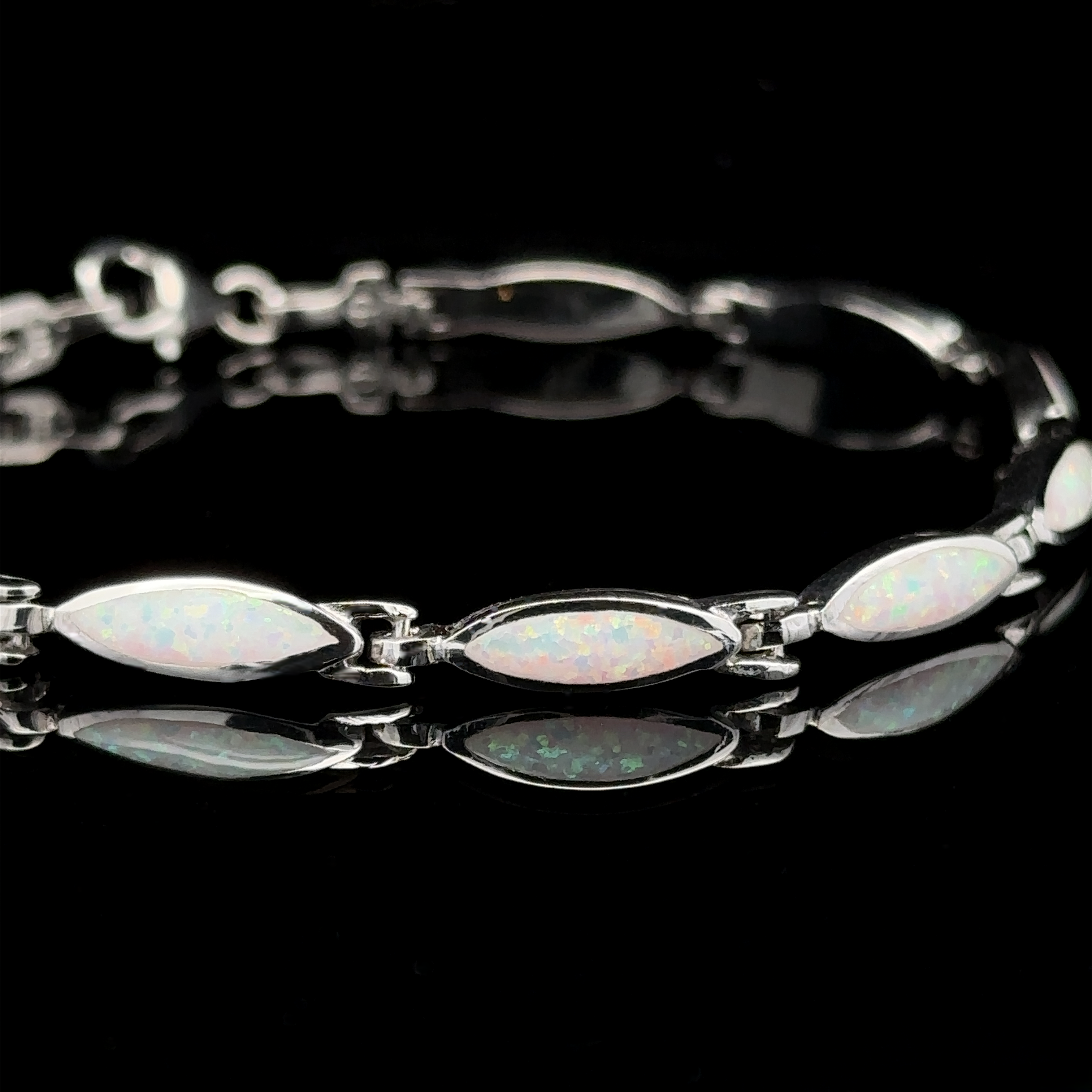 The Marquise Shaped Lab-Created Opal Bracelet, showcasing a contemporary aesthetic with silver and marquise-shaped lab-created opal gemstones, is elegantly displayed against a black background, reflecting light beautifully.