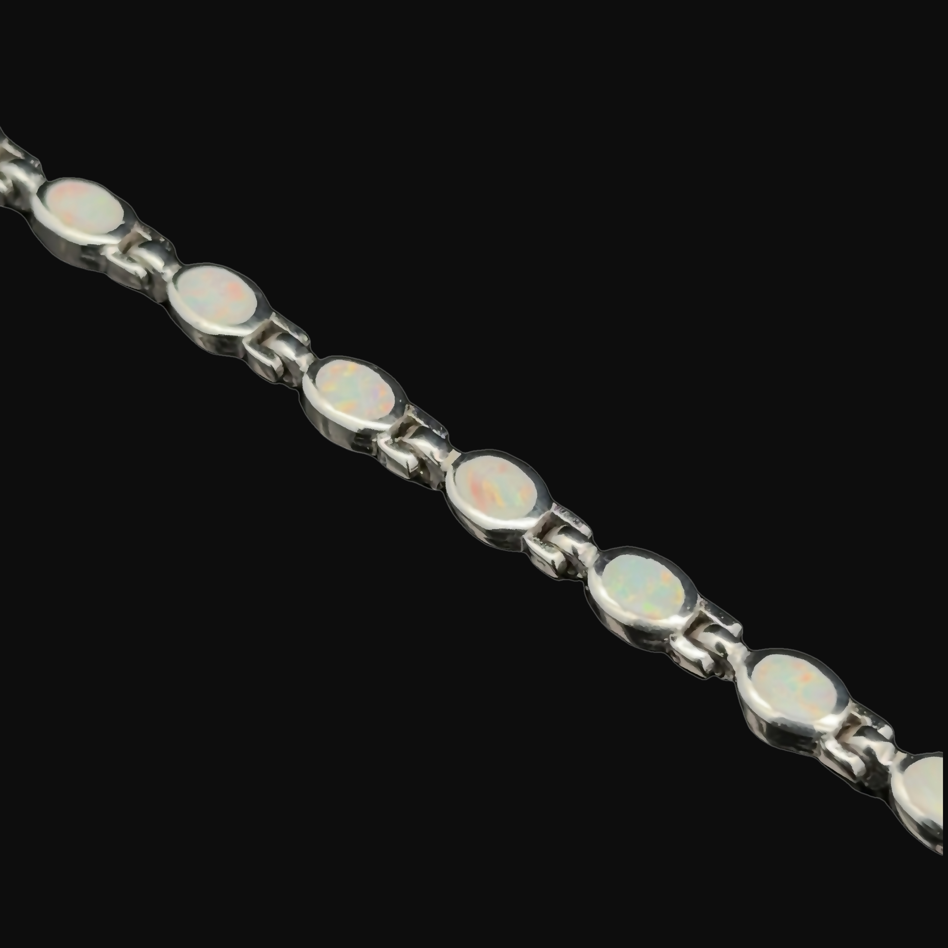 The Oval Lab-Created Opal Bracelet, consisting of multiple oval lab-created opal stones linked together against a black background, is an elegant piece of jewelry that is sure to captivate.