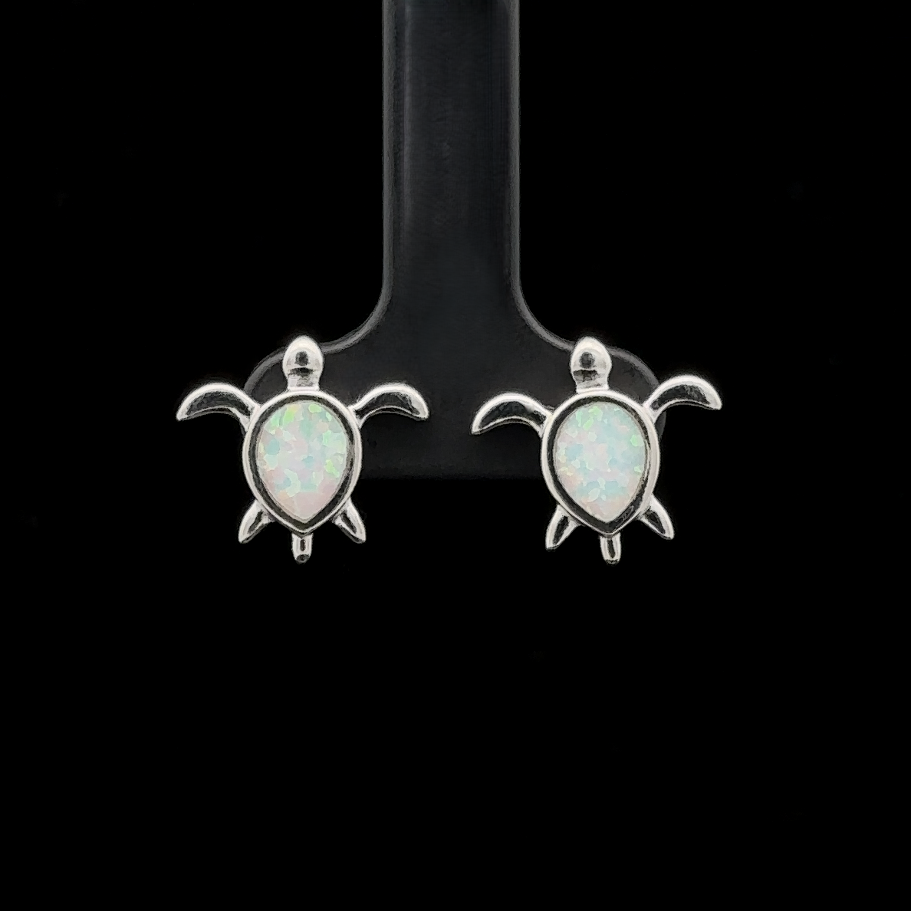 The Simple Lab-Created Opal Turtle Studs, a pair of small sterling silver sea turtle stud earrings featuring lab-created opal stones, are displayed against a black background.