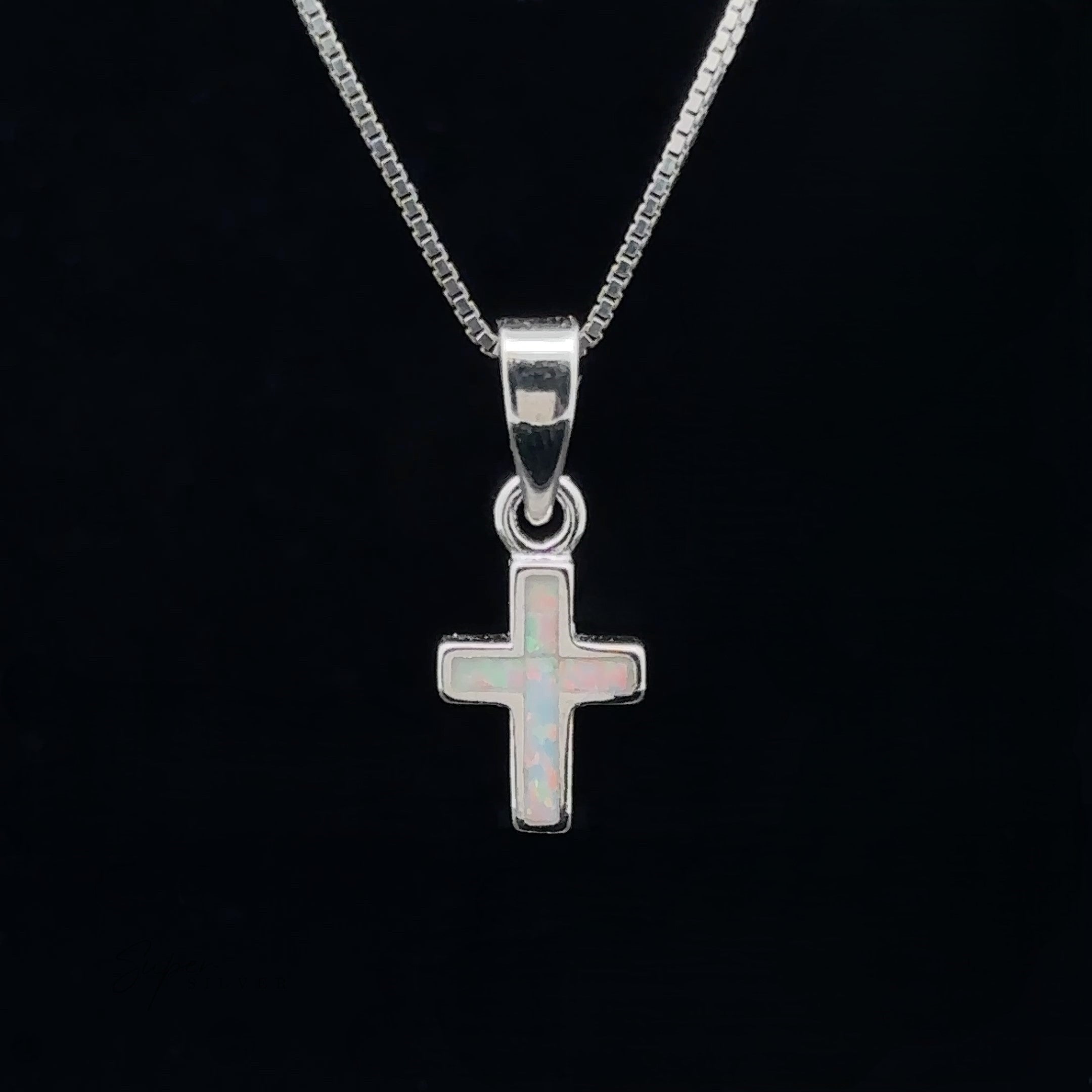 A Lab-Created Opal Cross Pendant, crafted from .925 Sterling Silver, glistens elegantly on a chain against a black background.